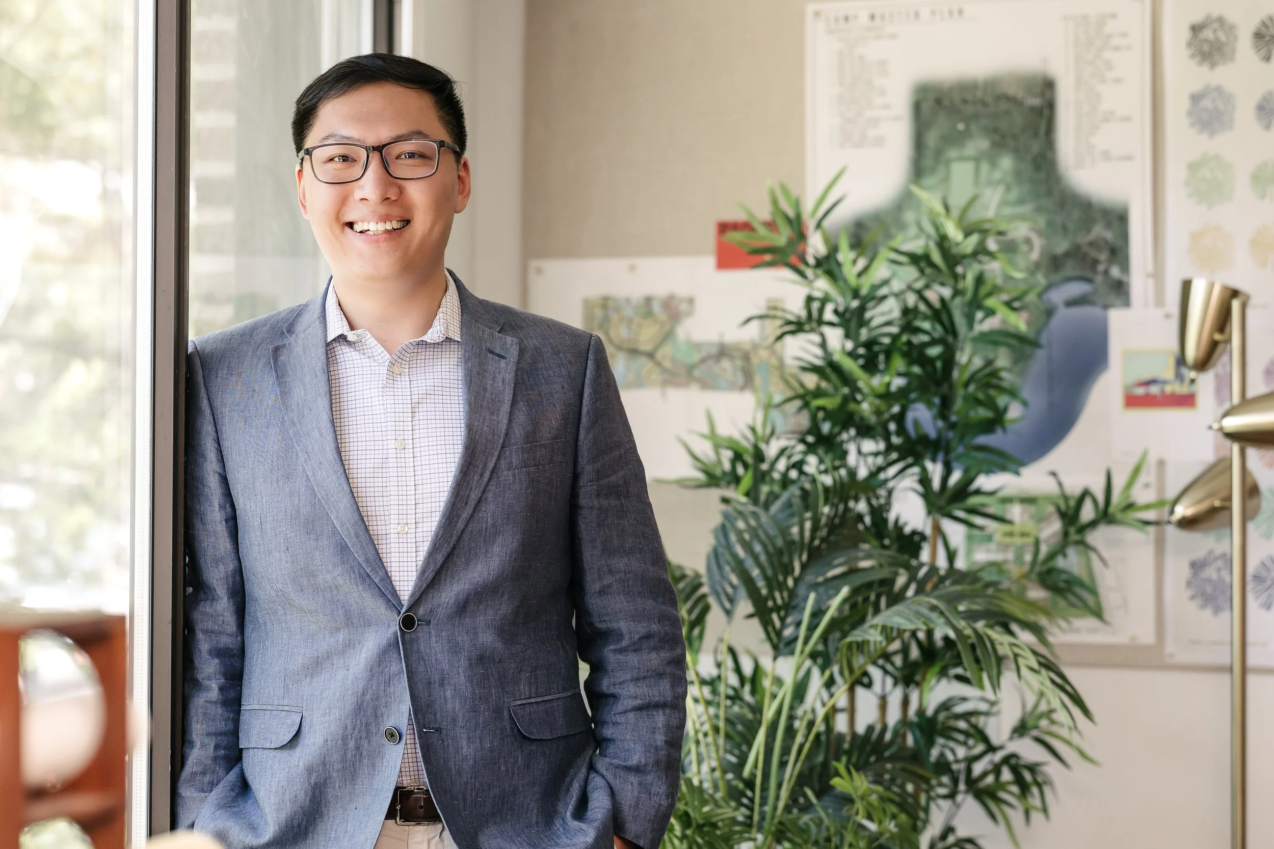 Yuchen Ding smiling and standing by a glass door, with a background of green plants and wall art.