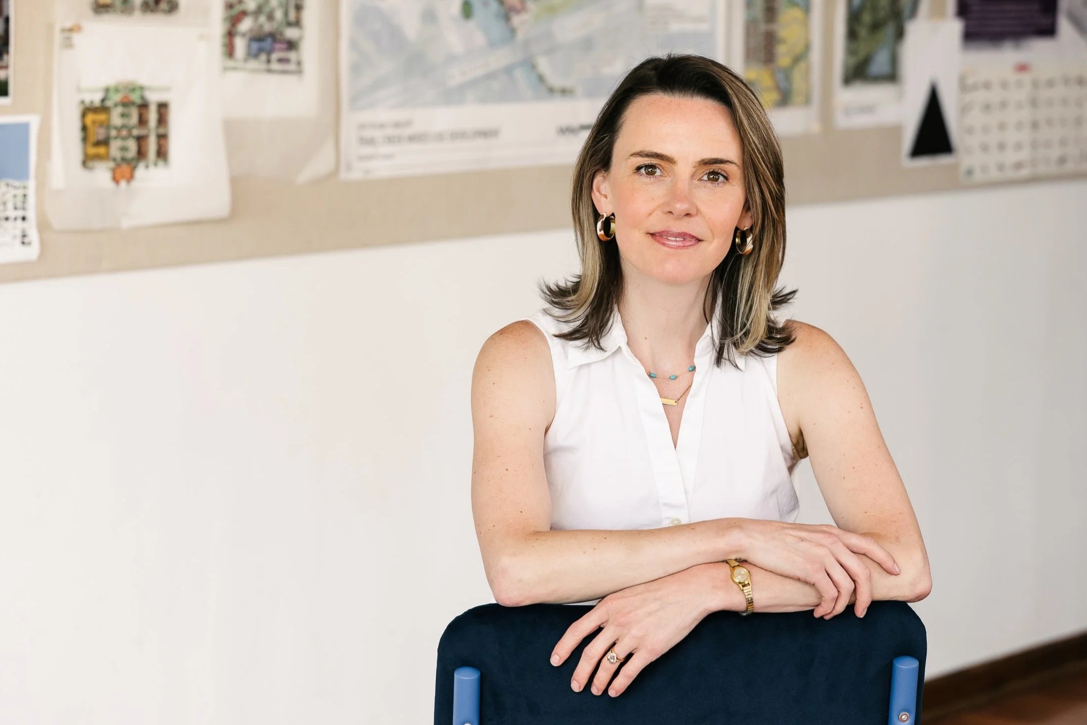 Erin Cigliano sitting at a desk with her arms crossed, in an office with maps and papers on the bulletin board in the background.