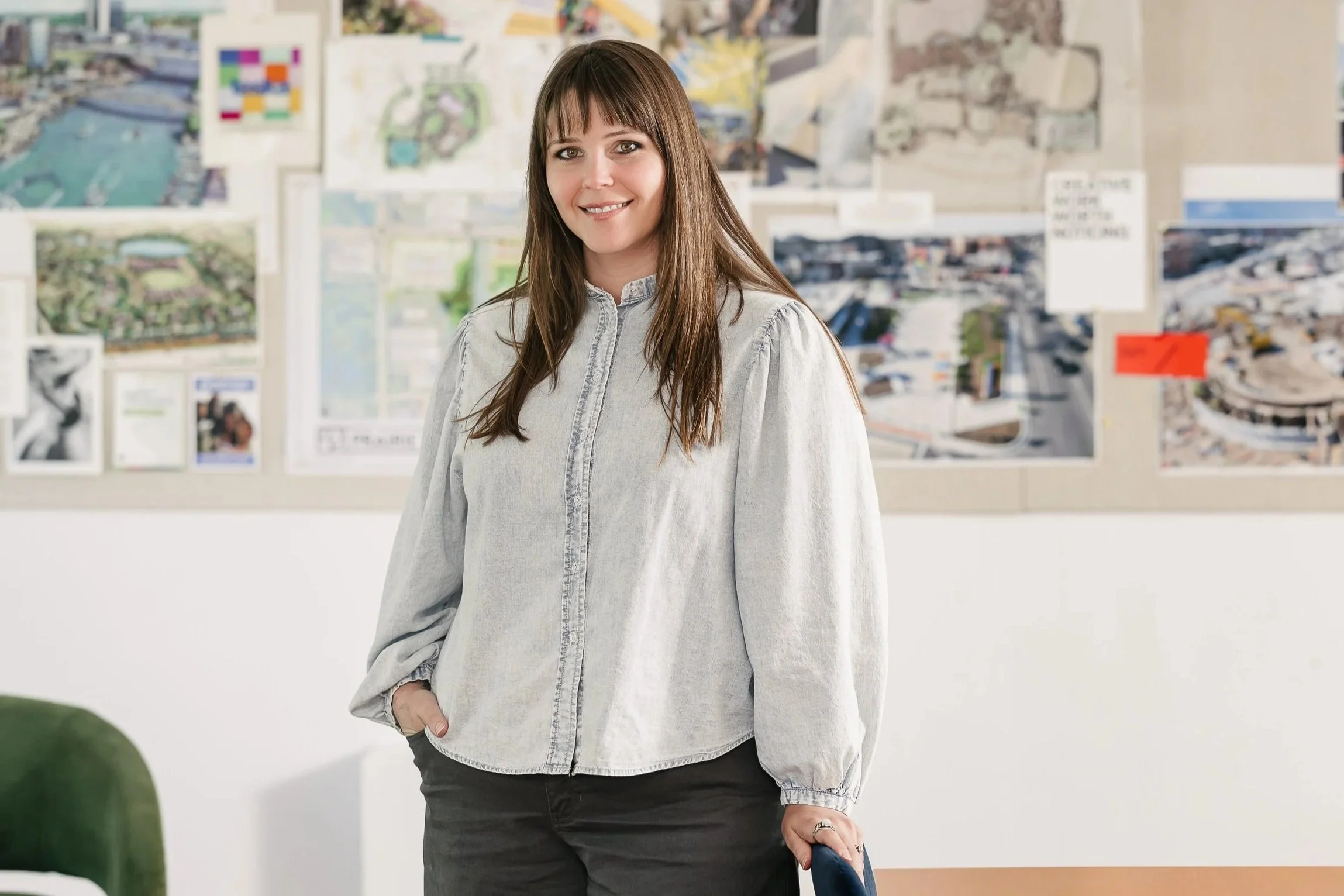 Lacey Carlson standing indoors in front of a wall with various architectural plans and artwork.