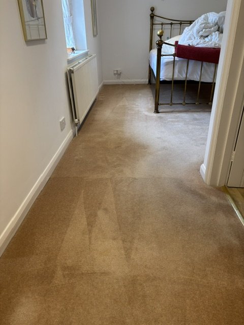 A bedroom doorway with a carpeted floor, part of a bed with white bedding and a red throw, and a window with natural light.
