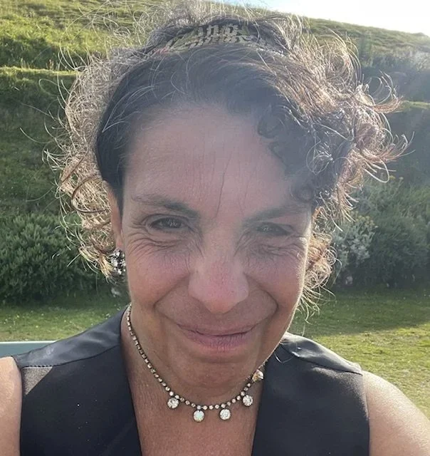 Photo of Charlotte Levene wearing a black sleeveless top standing in a green field with bushes in the background and a light sky