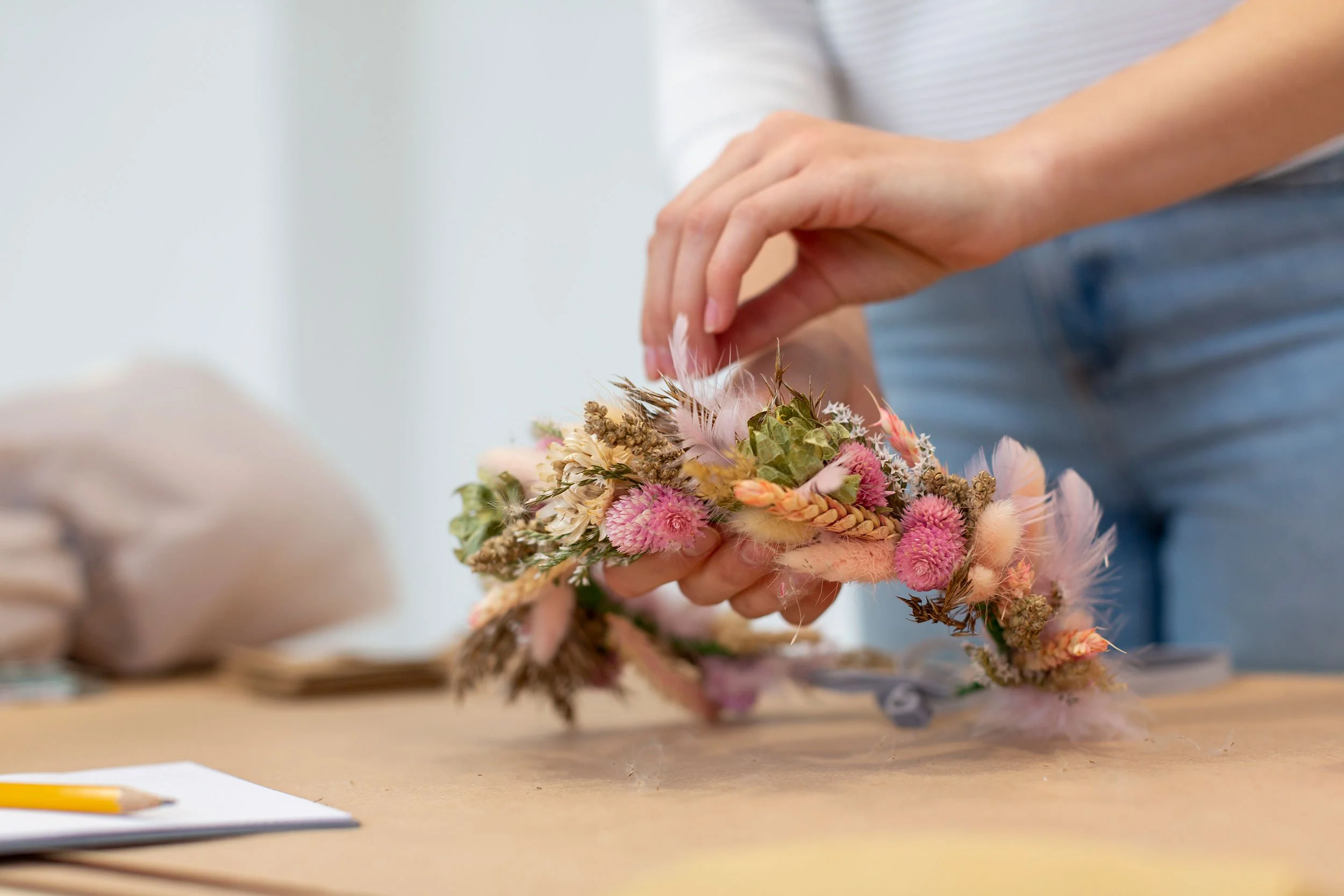 Person creating a floral arrangement with dried pink, green, and beige flowers.