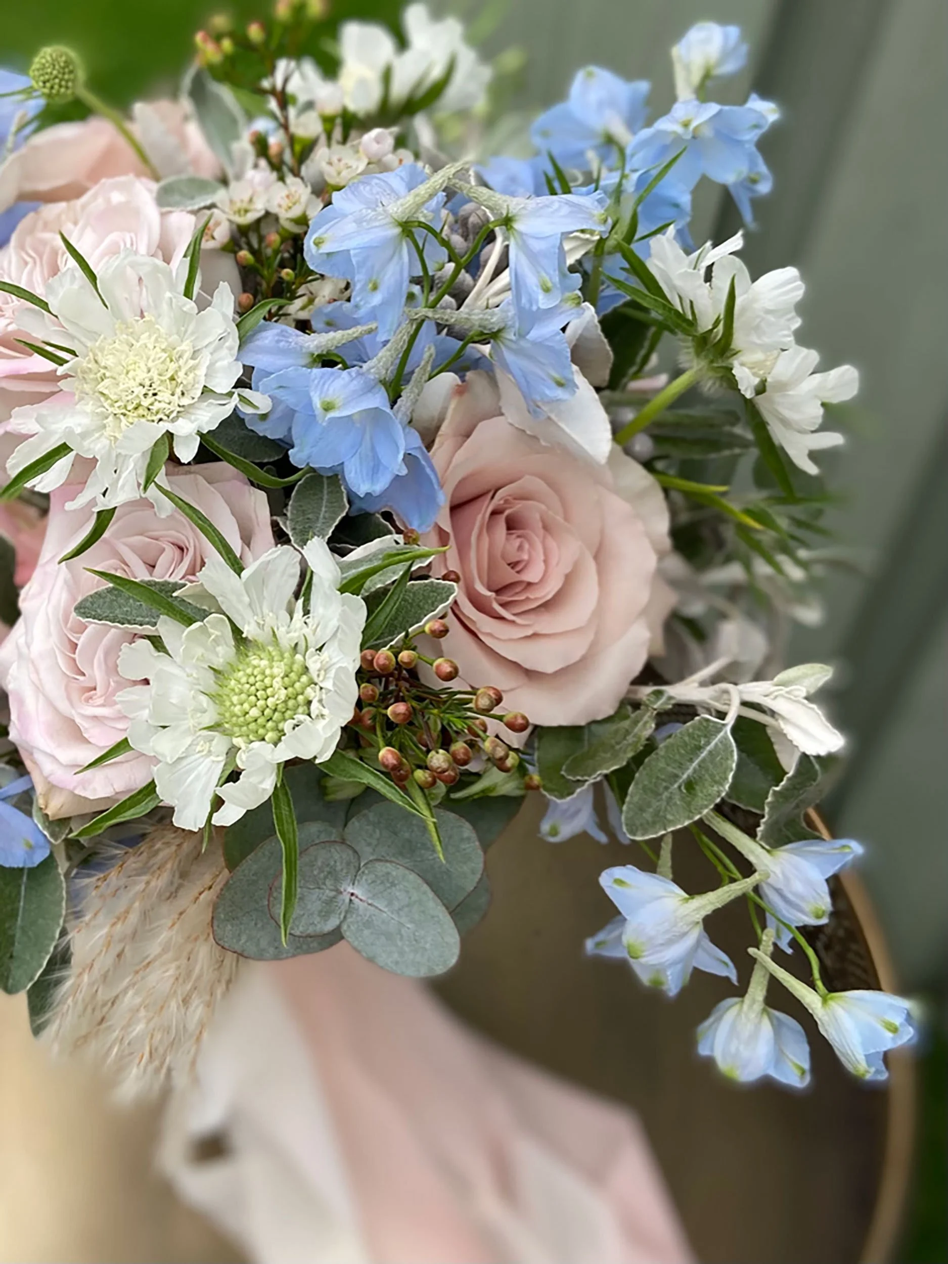 Close-up of a bouquet with pale pink roses, white and blue flowers, and greenery including eucalyptus leaves.
