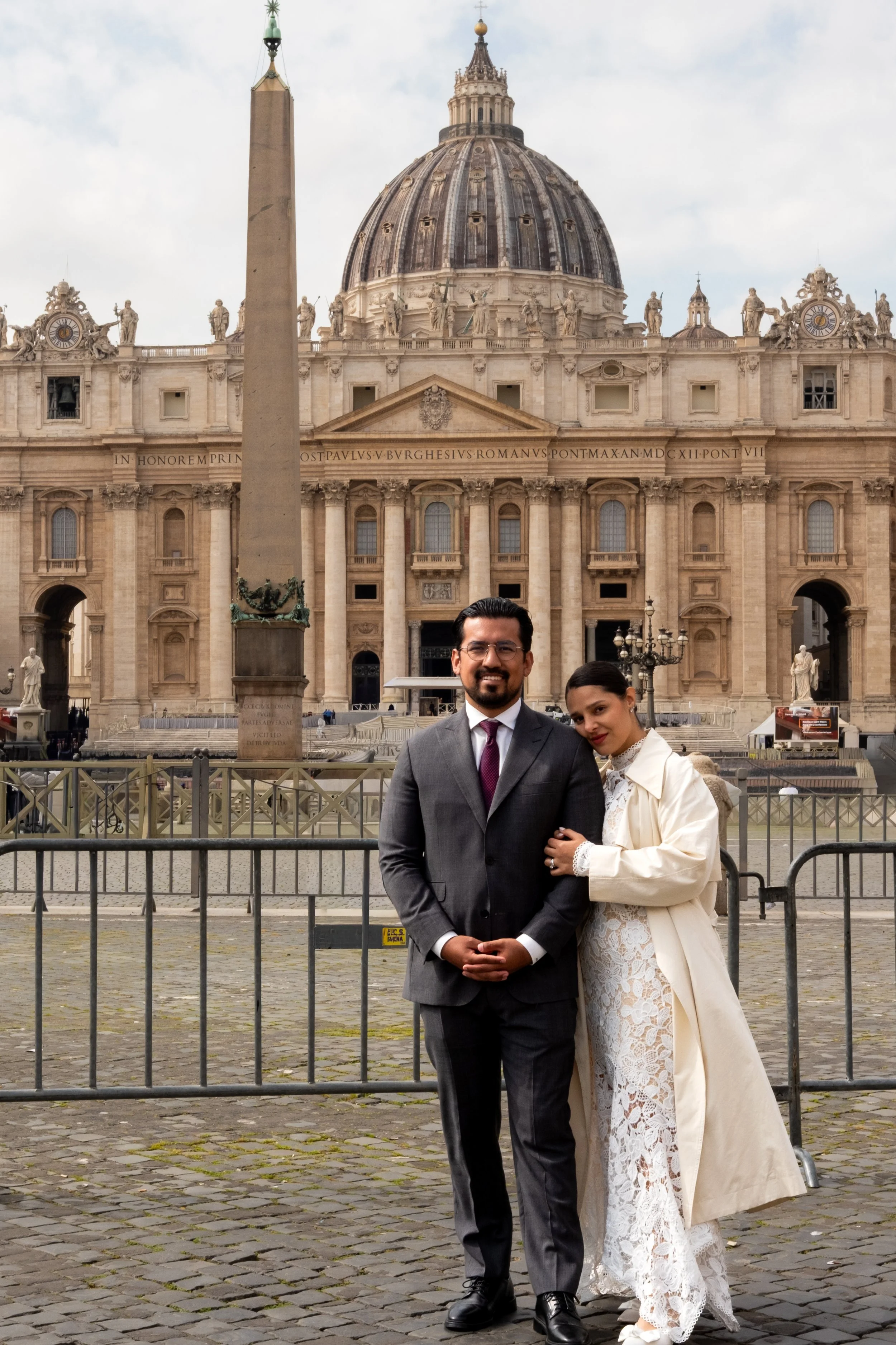 A man and woman standing close together, dressed formally, in front of St. Peter's Basilica in Vatican City.