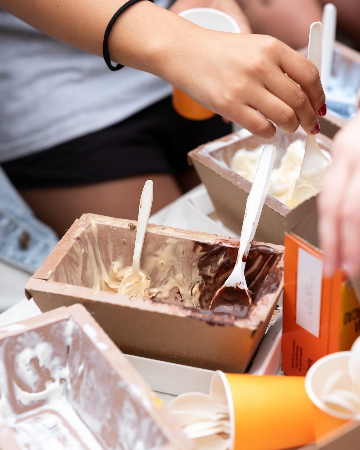 A person scooping gelato from a cardboard container with multiple flavors at a villa