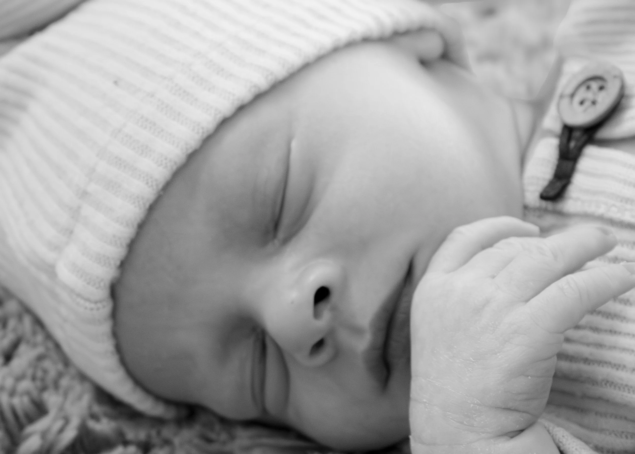 Close-up of a baby’s face with eyes closed, wearing a striped hat and lying on a blanket.