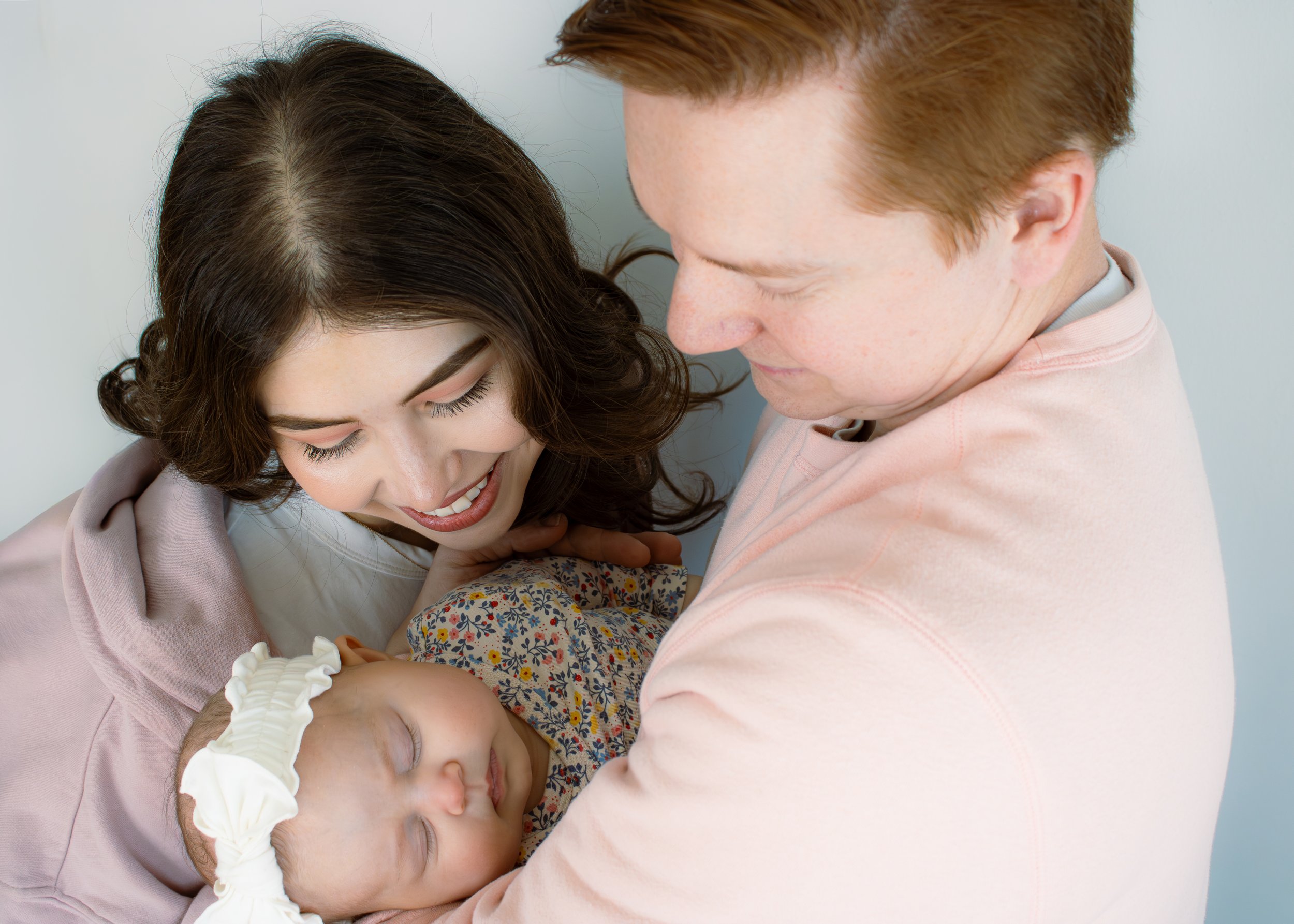 A woman and man sharing a tender moment with two sleeping children, one with a medical brace on their arm and a nasal tube, in a light-colored room.