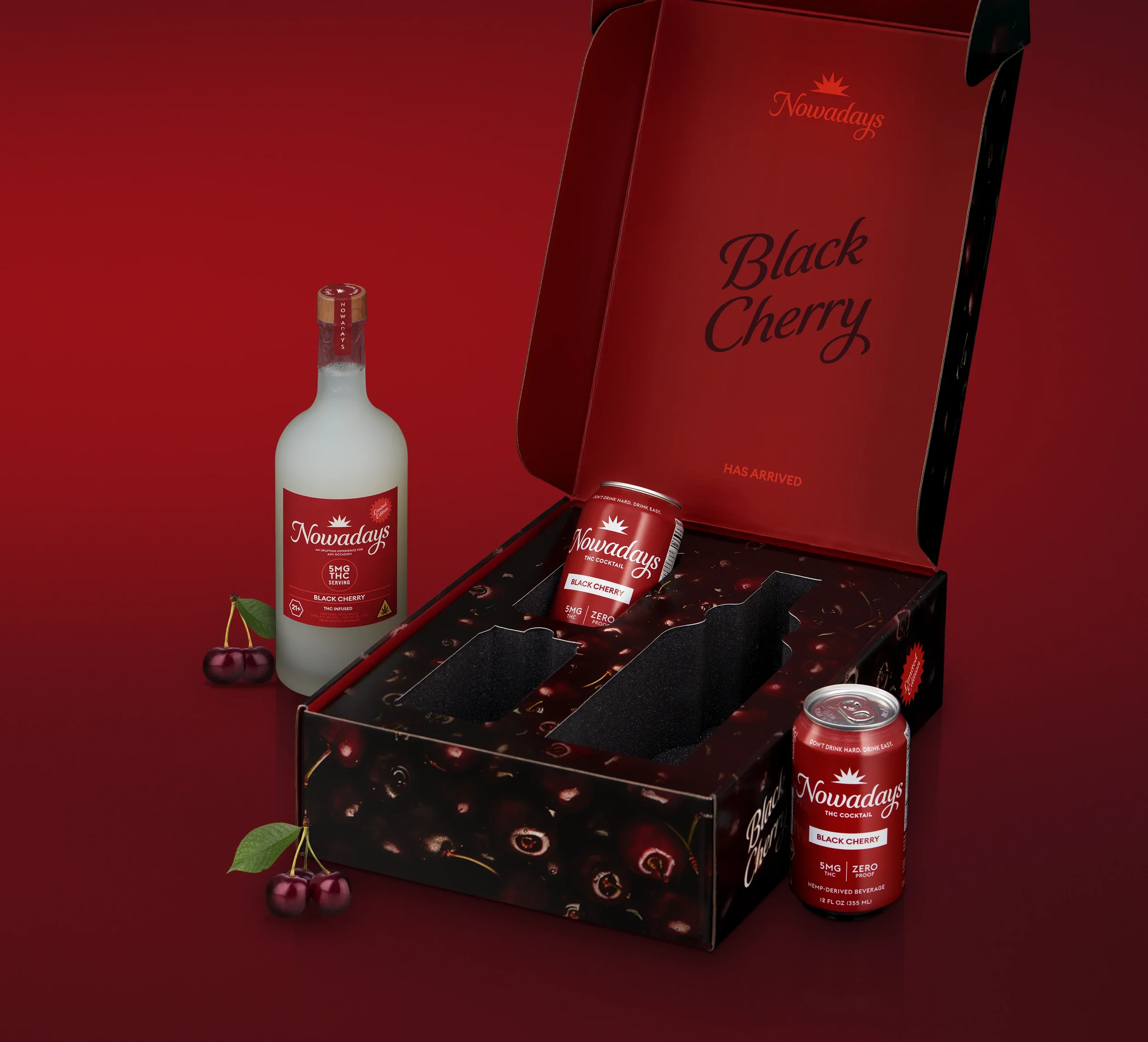 A black cherry flavored cannabis drink from Nowadays, with a red can and branding, next to a bottle and cherries with leaves, set against a red background and part of a black box display.