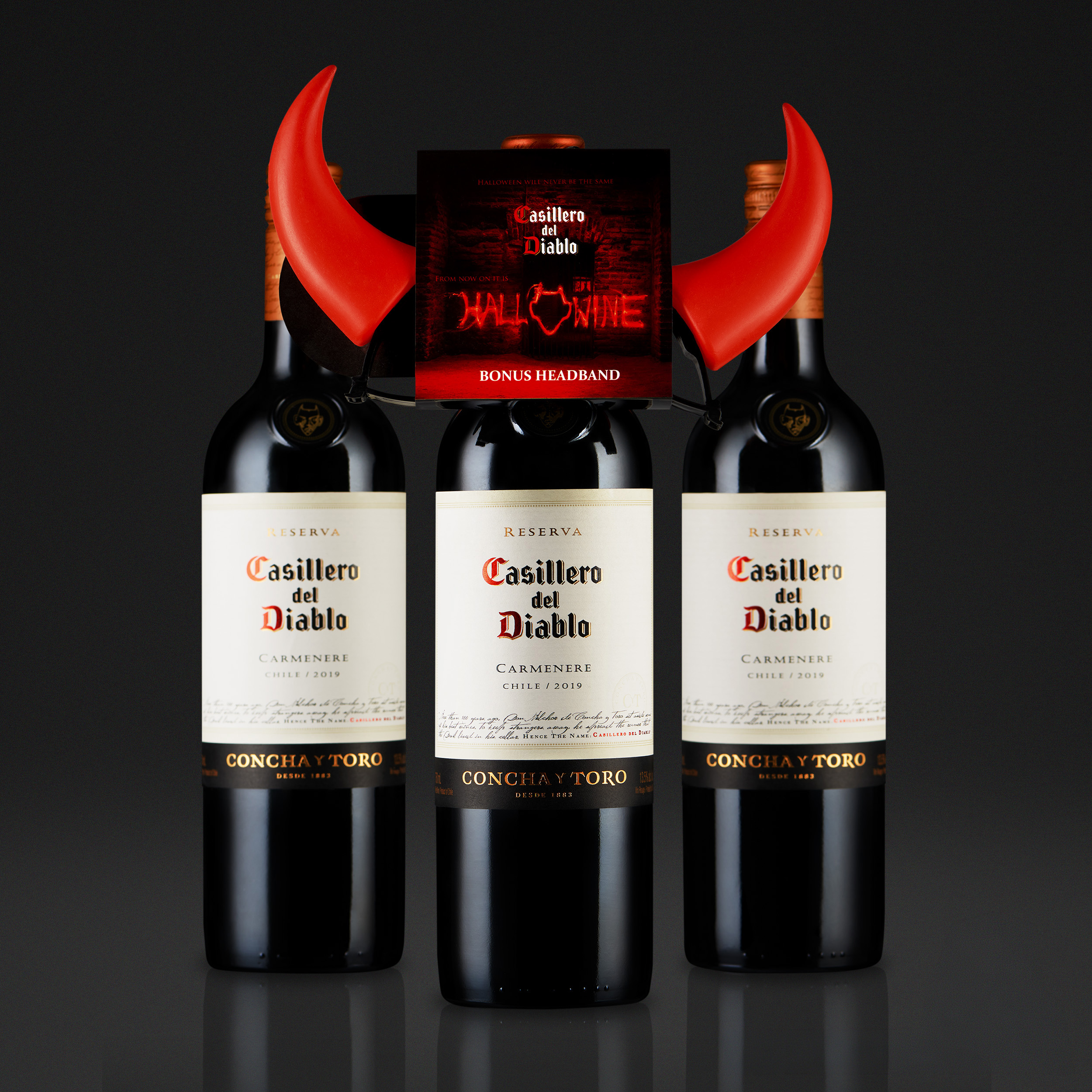 Three bottles of Casillero del Diablo wine with a red Halloween-themed headband featuring red horns in front of a black background.