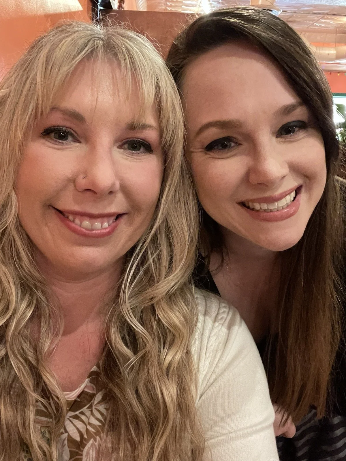 Two women smiling closely for a selfie in a warm indoor setting.