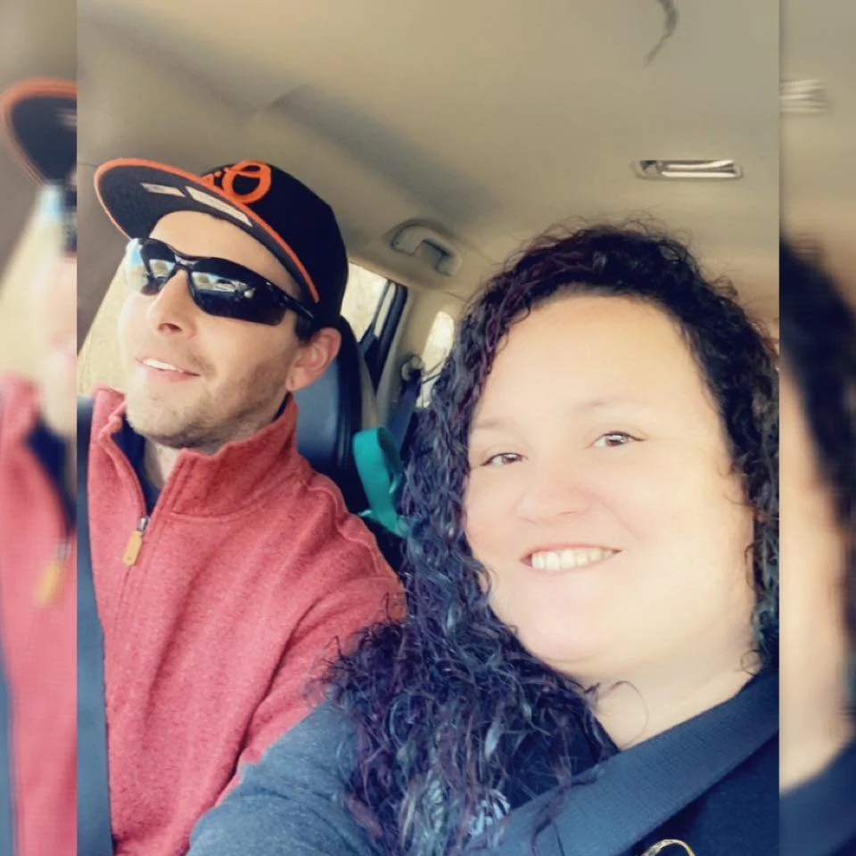 A man and woman taking a selfie inside a car, both smiling at the camera.