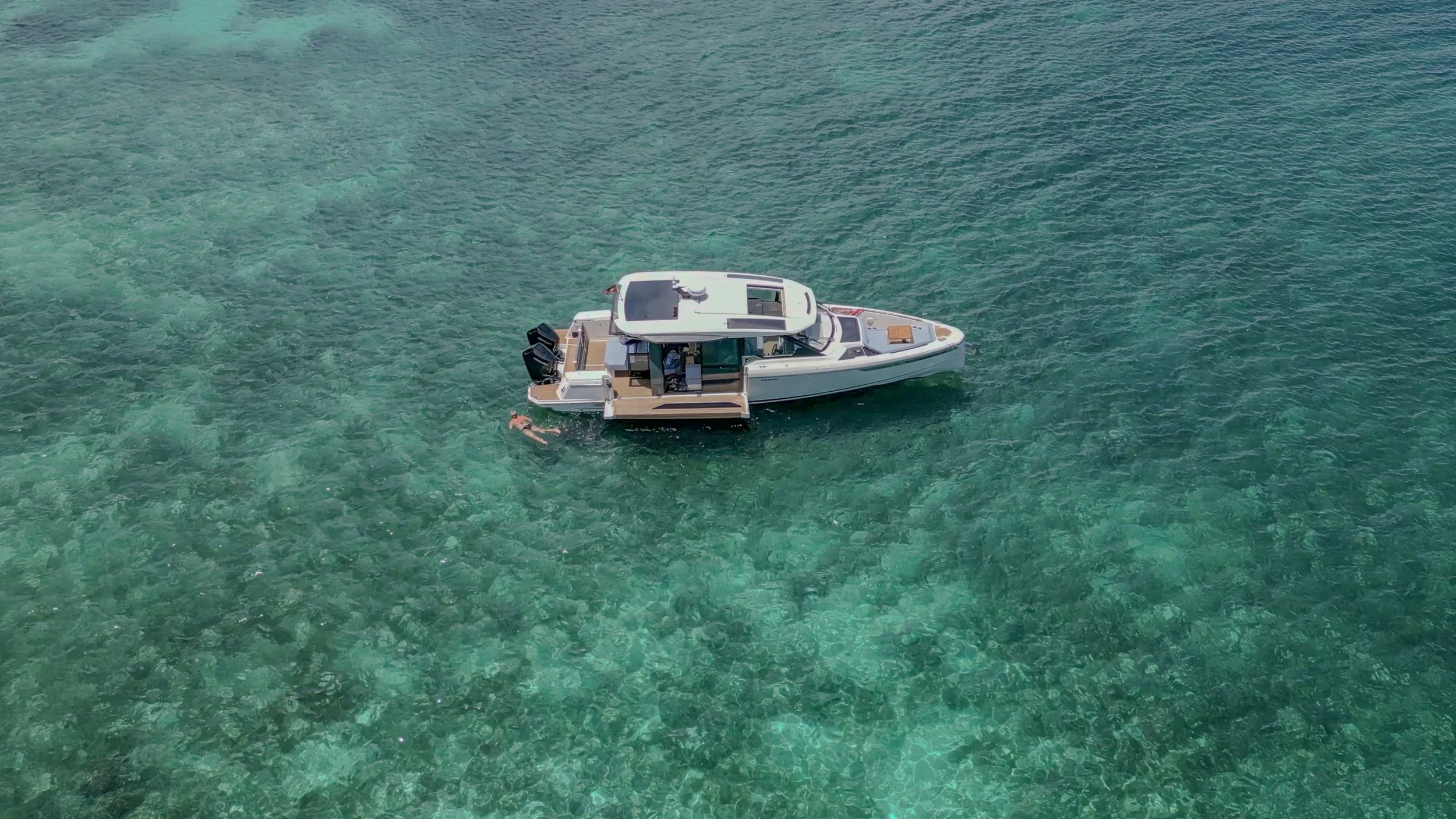 A boat floating on clear turquoise water with a person swimming nearby.