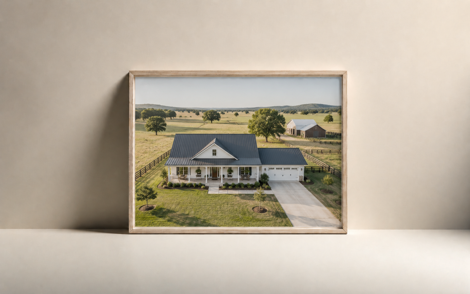 Framed photograph of a white house with a gray roof on a green lawn with young trees, surrounded by a wooden fence, on a farm with fields, trees, and a barn in the background.