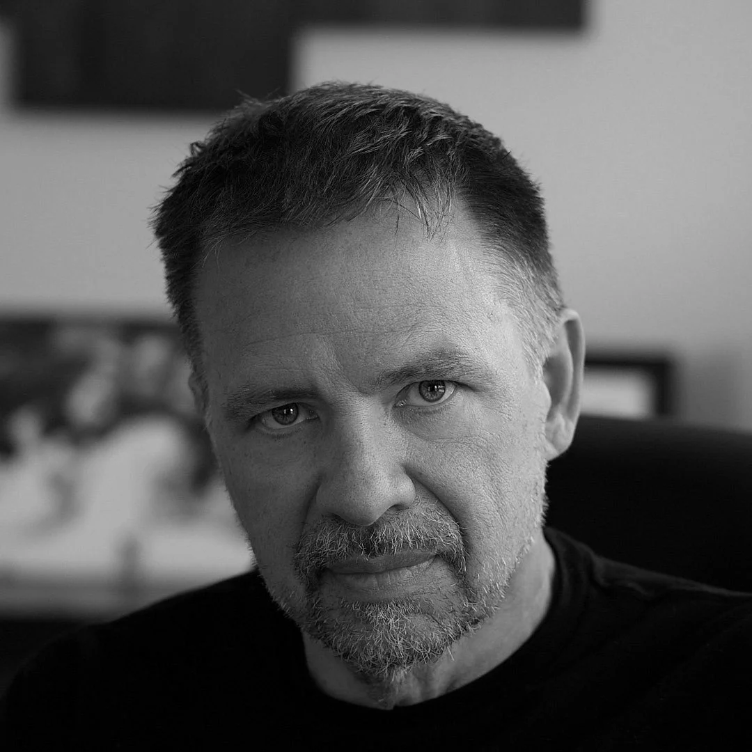 Black and white close-up portrait of a middle-aged man with short hair and a beard, looking directly at the camera.