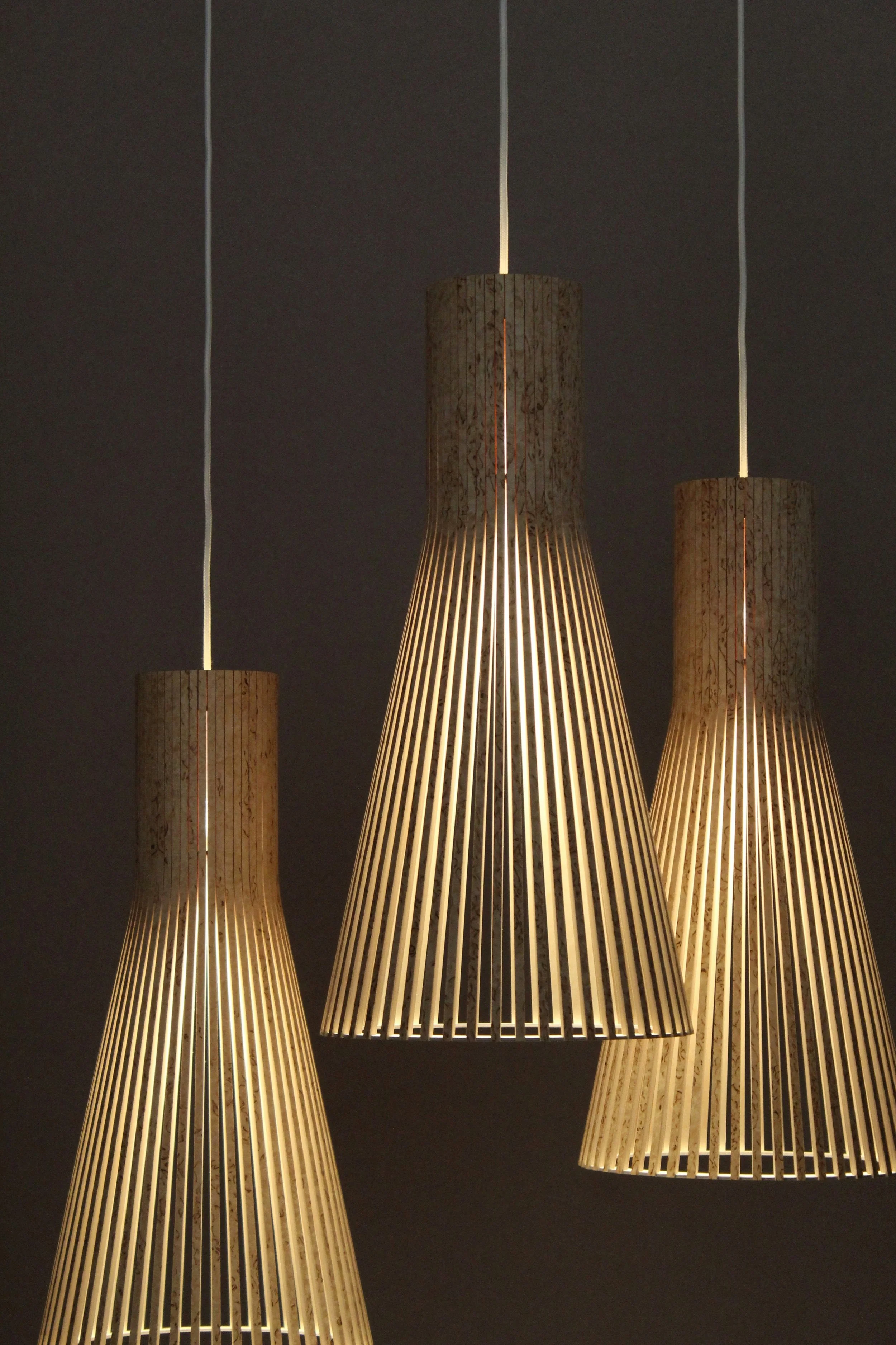 Four wooden pendant lamps with vertical slats hanging against a dark background.