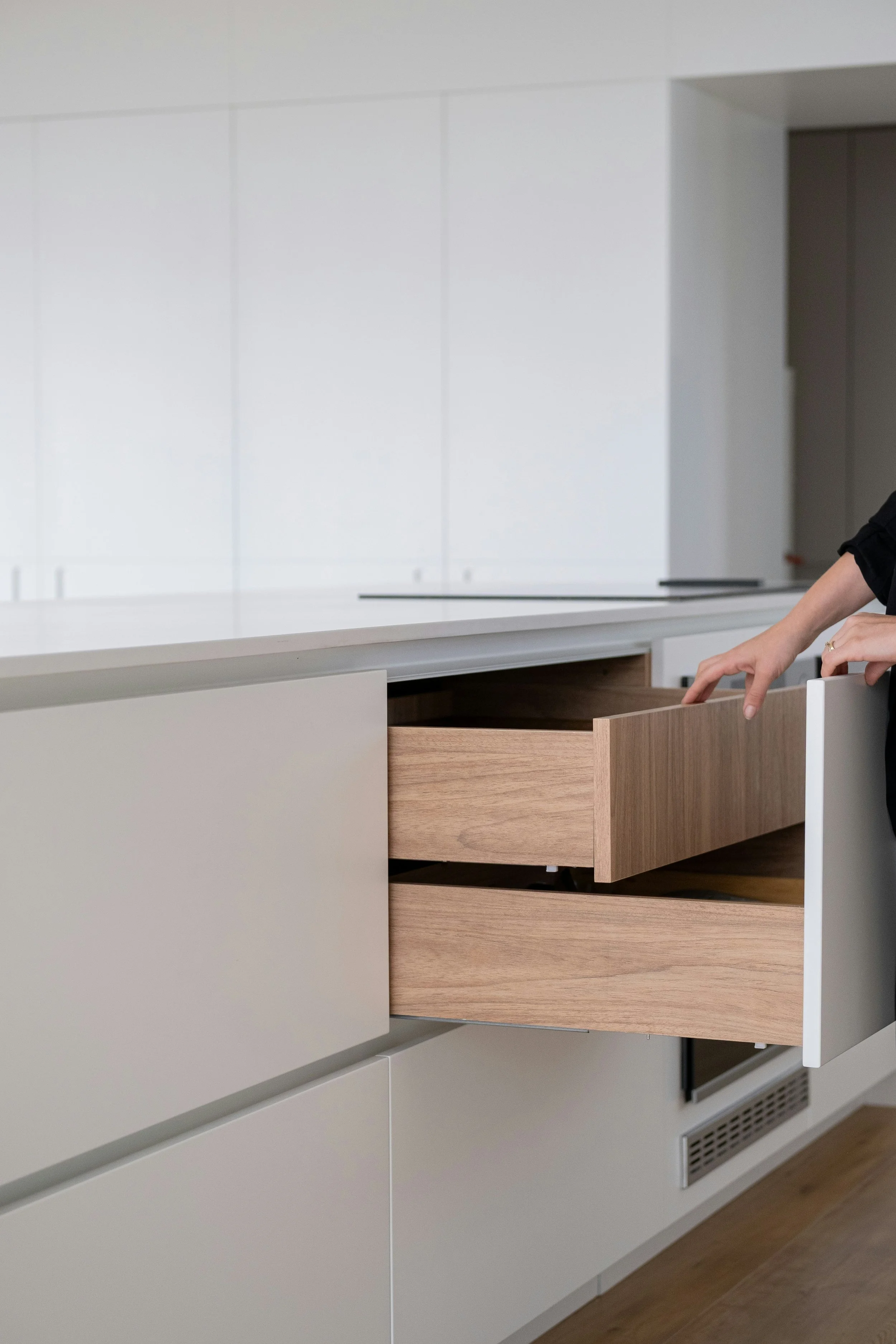 A modern kitchen with white cabinets and wooden drawers, with one drawer being pulled out by a person.