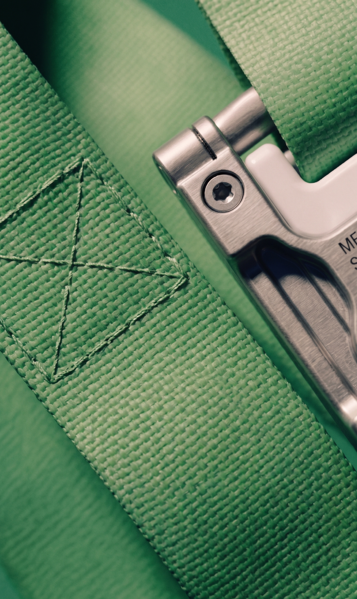 Close-up of a metal buckle and green woven strap with stitched end.
