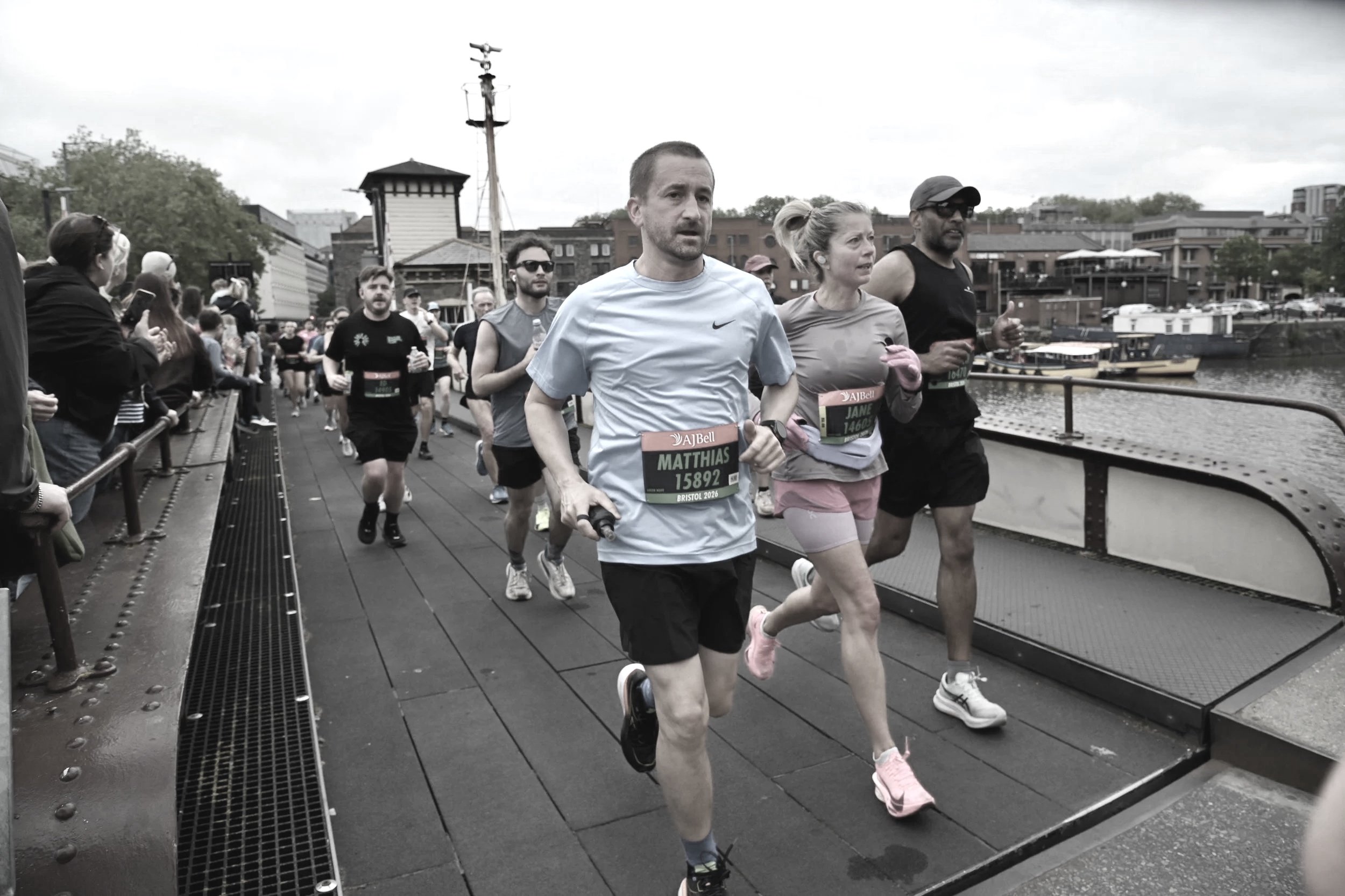 Group of runners participating in a marathon or running event along a waterfront with spectators cheering on the side.