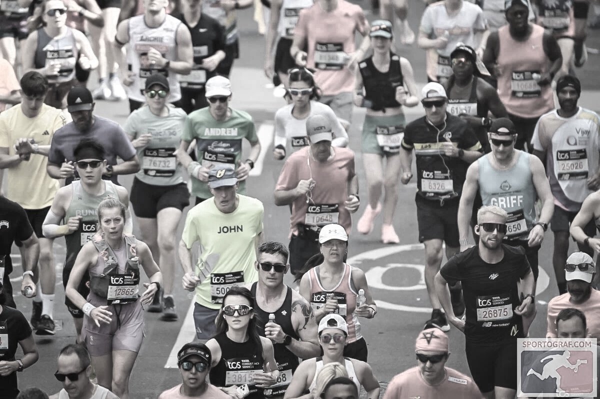 Crowd of marathon runners participating in a race, wearing athletic clothing, with some wearing sunglasses and hats.