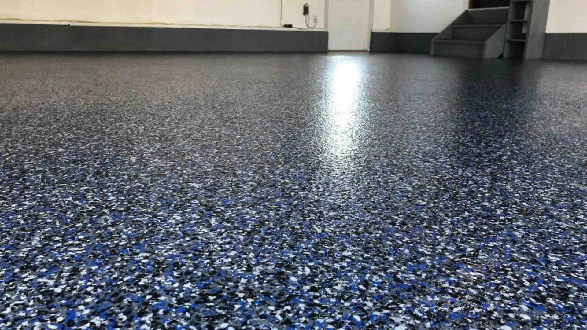A shiny black and blue speckled epoxy flooring in an indoor room with stairs on the right and an electrical outlet on the wall.