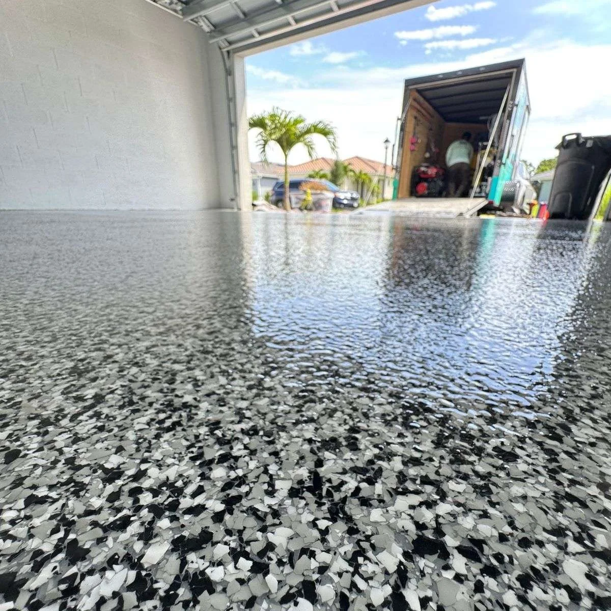 Polished terrazzo floor in garage with an open door leading outside where a moving truck and parked cars are visible.