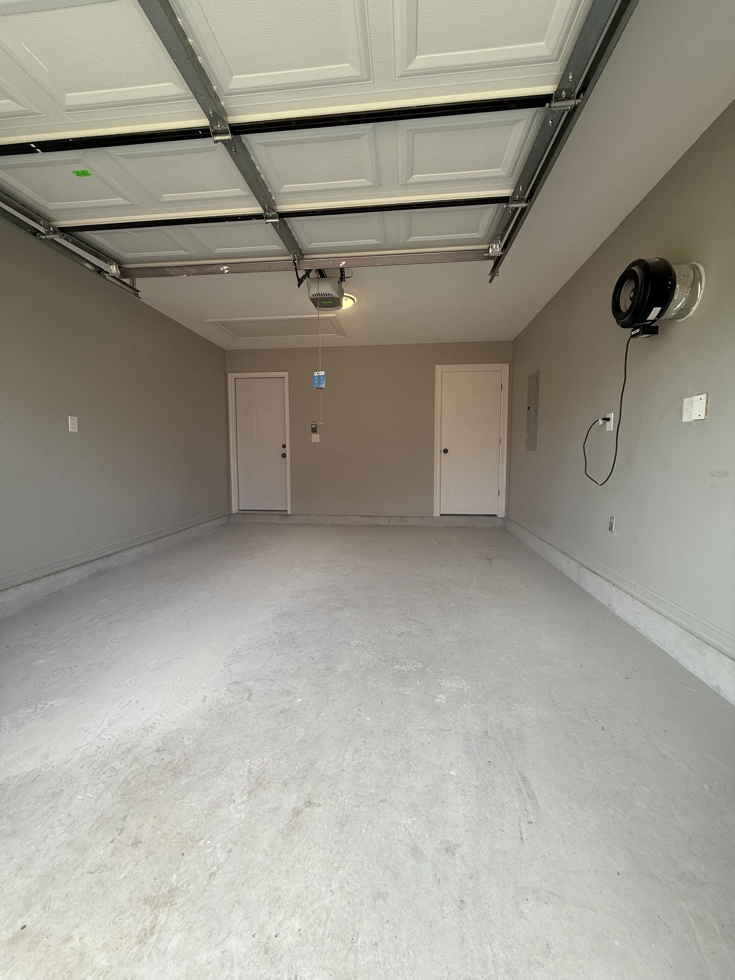 Empty garage with a closed ceiling door, two closed doors, and a speaker mounted on the wall.