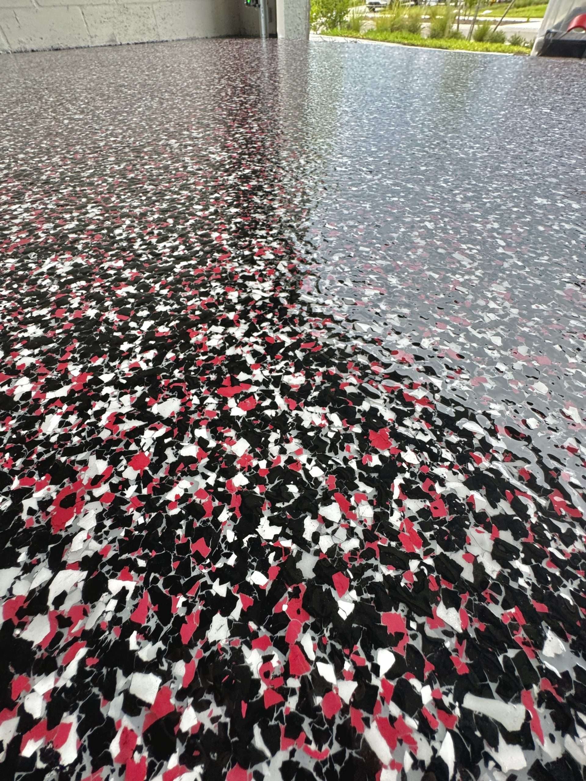Close-up photo of a terrazzo floor with black, white, red, and gray chips in various sizes, leading to an outdoor view with grass and a parking lot.