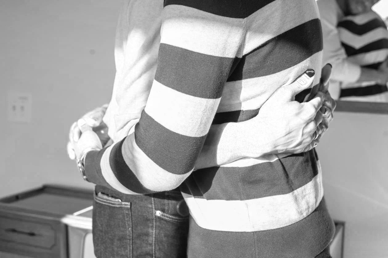 A person wearing a striped sweater holds their chest with one hand, standing indoors.