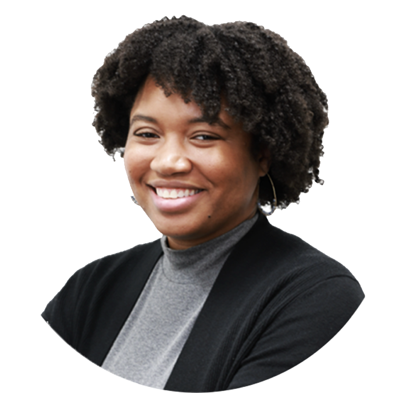 Portrait of a smiling African American woman with natural curly hair, wearing a gray turtleneck and black blazer.