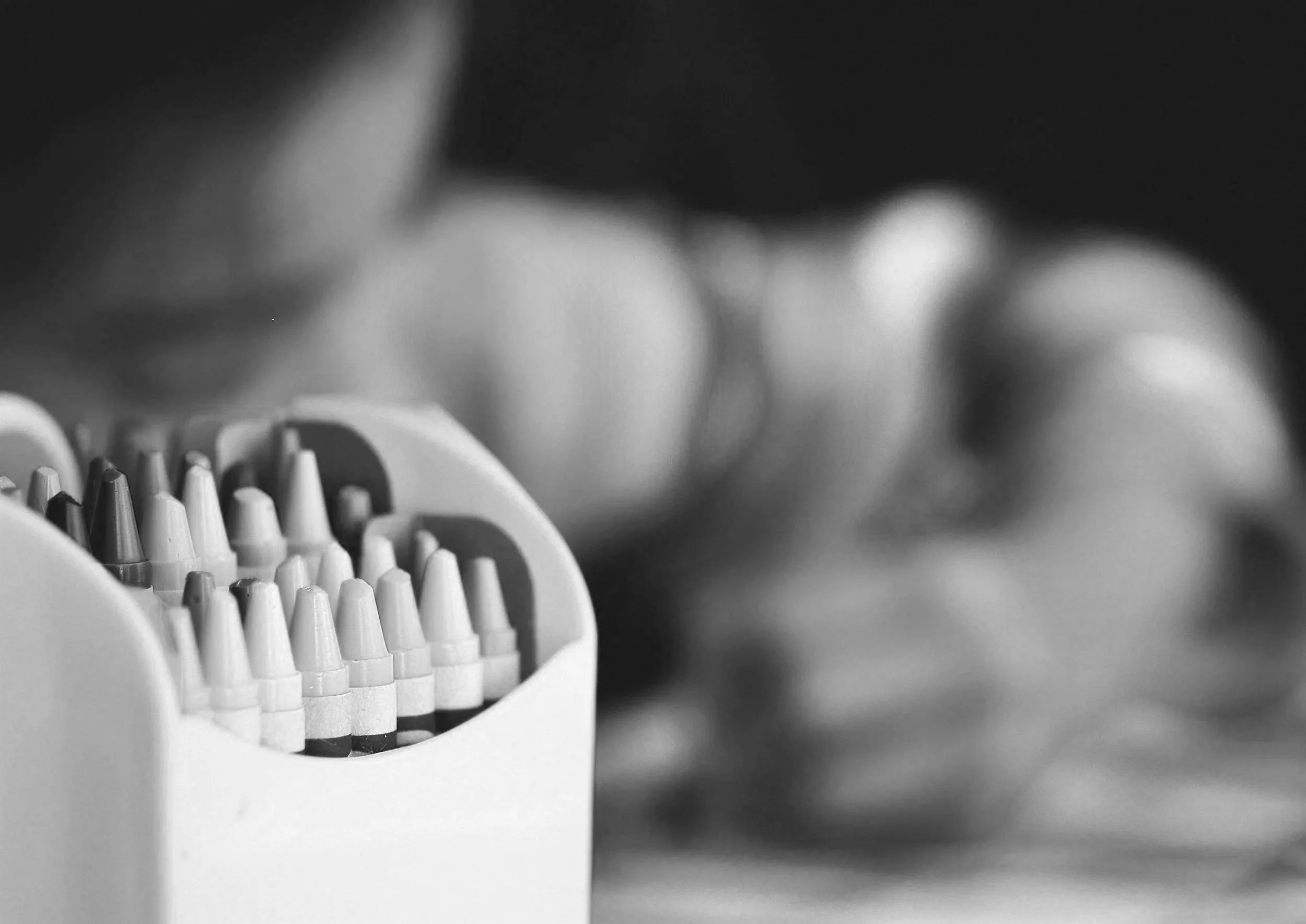 A black and white photo of a round plastic container filled with small, conical objects that appear to be tips or nozzles. The container is in the foreground, with slightly blurred out background.