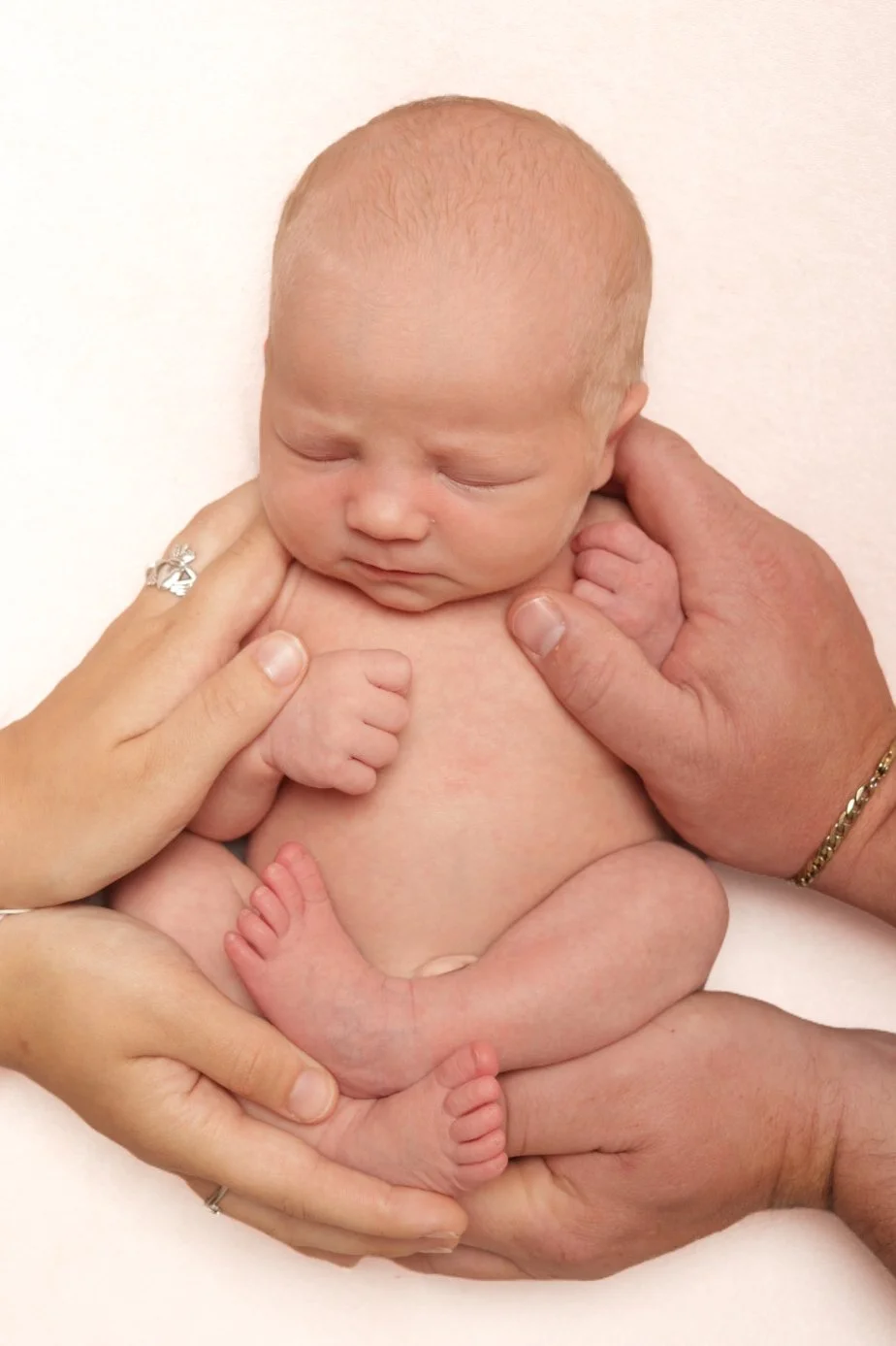 Professional newborn photography in Staffordshire showing a sleeping newborn baby cradled in parents' hands.
