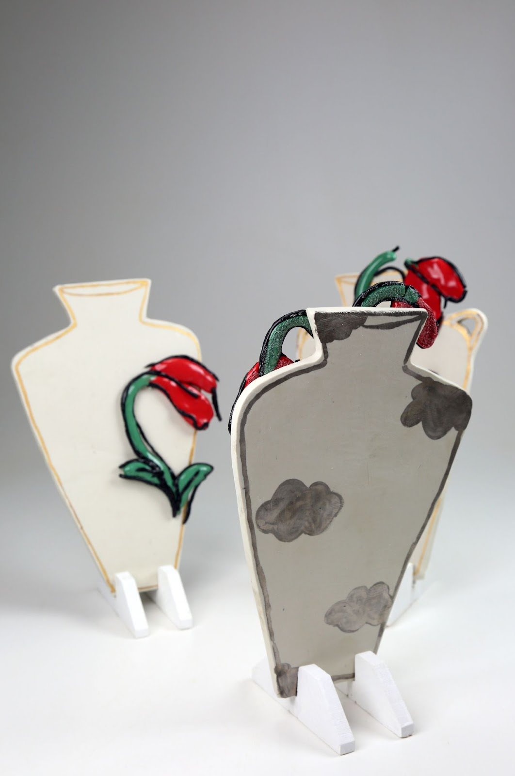Decorative figures of vases with flowers, painted on cardboard or similar material, displayed on white stands.