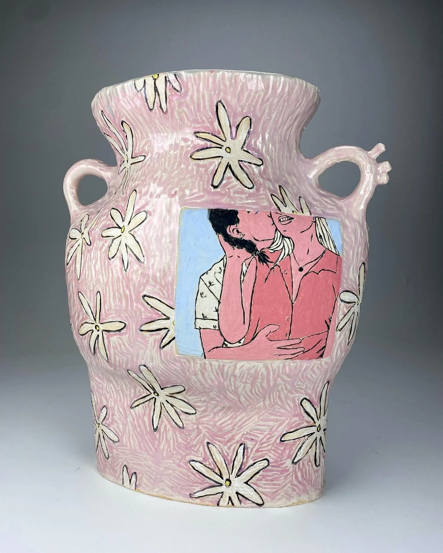 Decorative ceramic vase with pink background, white daisy flower patterns, and a colorful illustration of a couple kissing on the front.