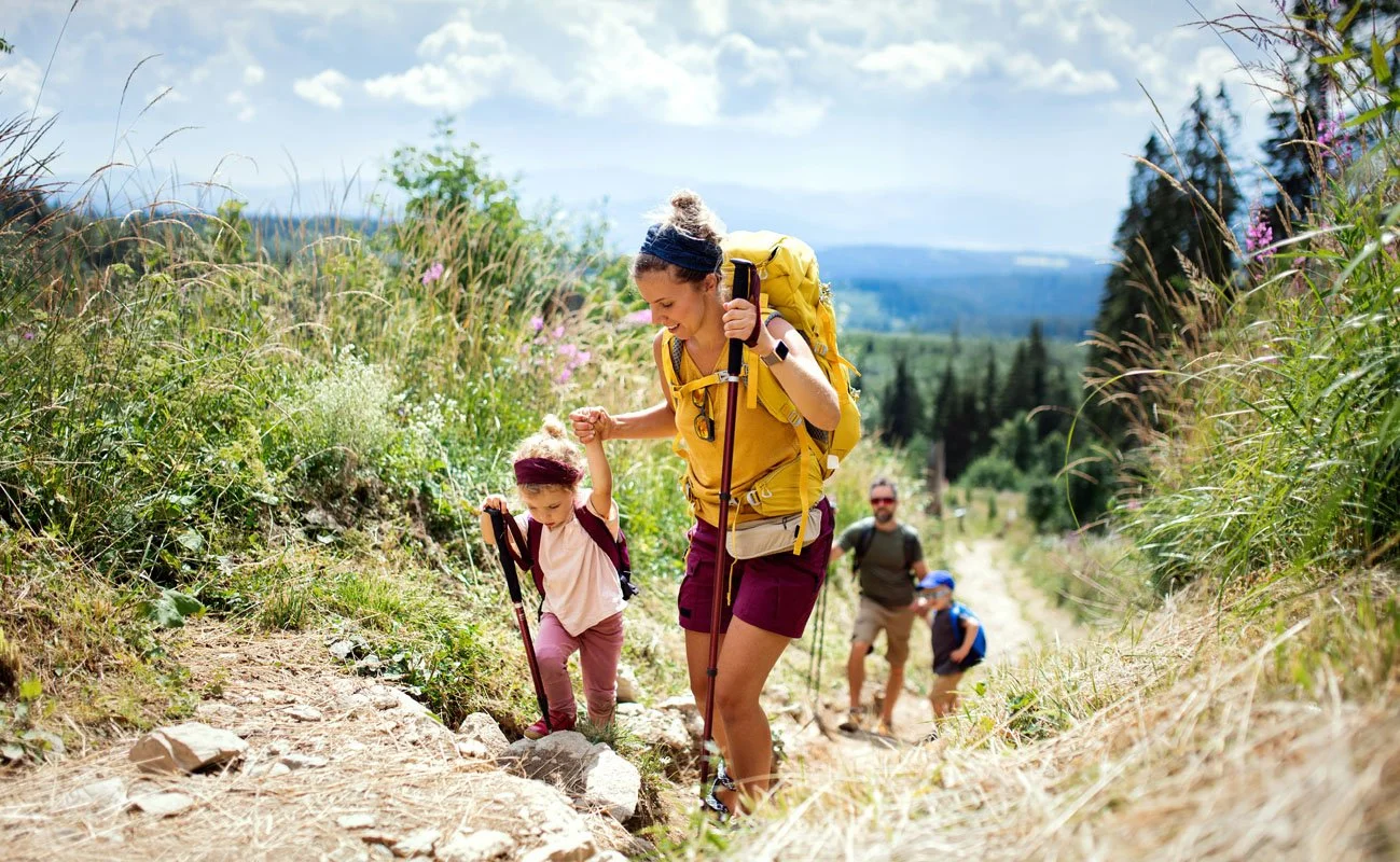 A woman and her young child hiking up a trail with backpacks, holding hands.