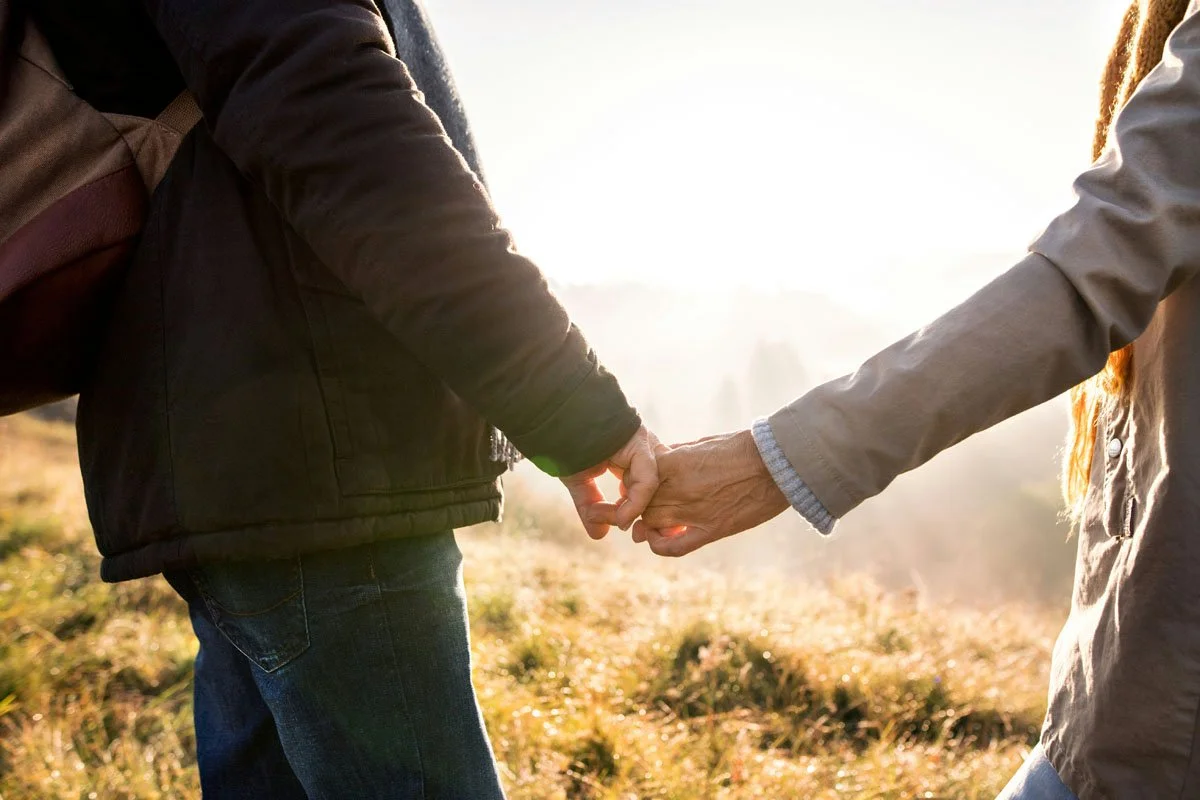 Two people holding hands outdoors with sunlight in the background.
