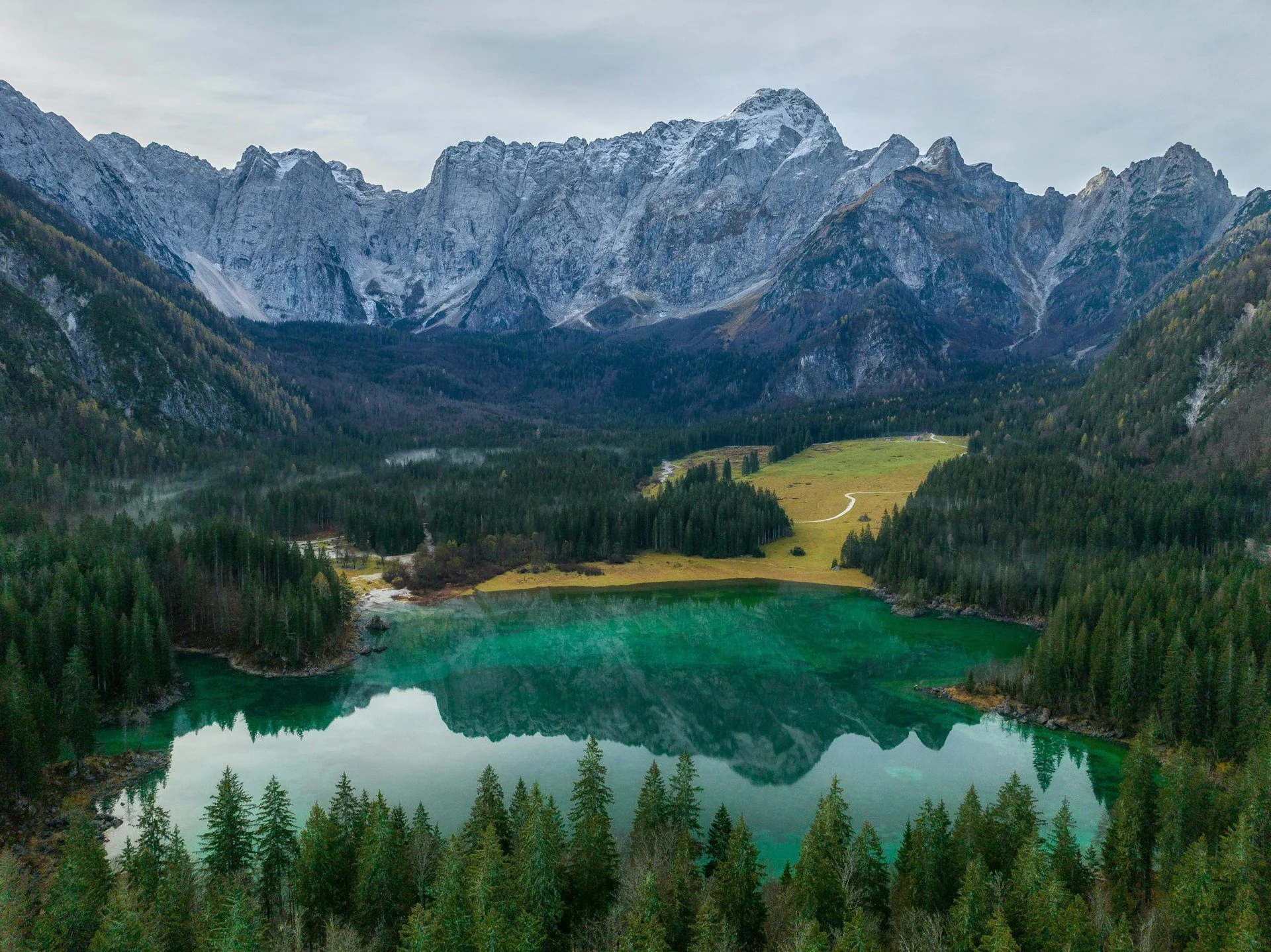 Mountain range with snow-capped peaks, dense evergreen forest, and a calm turquoise lake at the base.