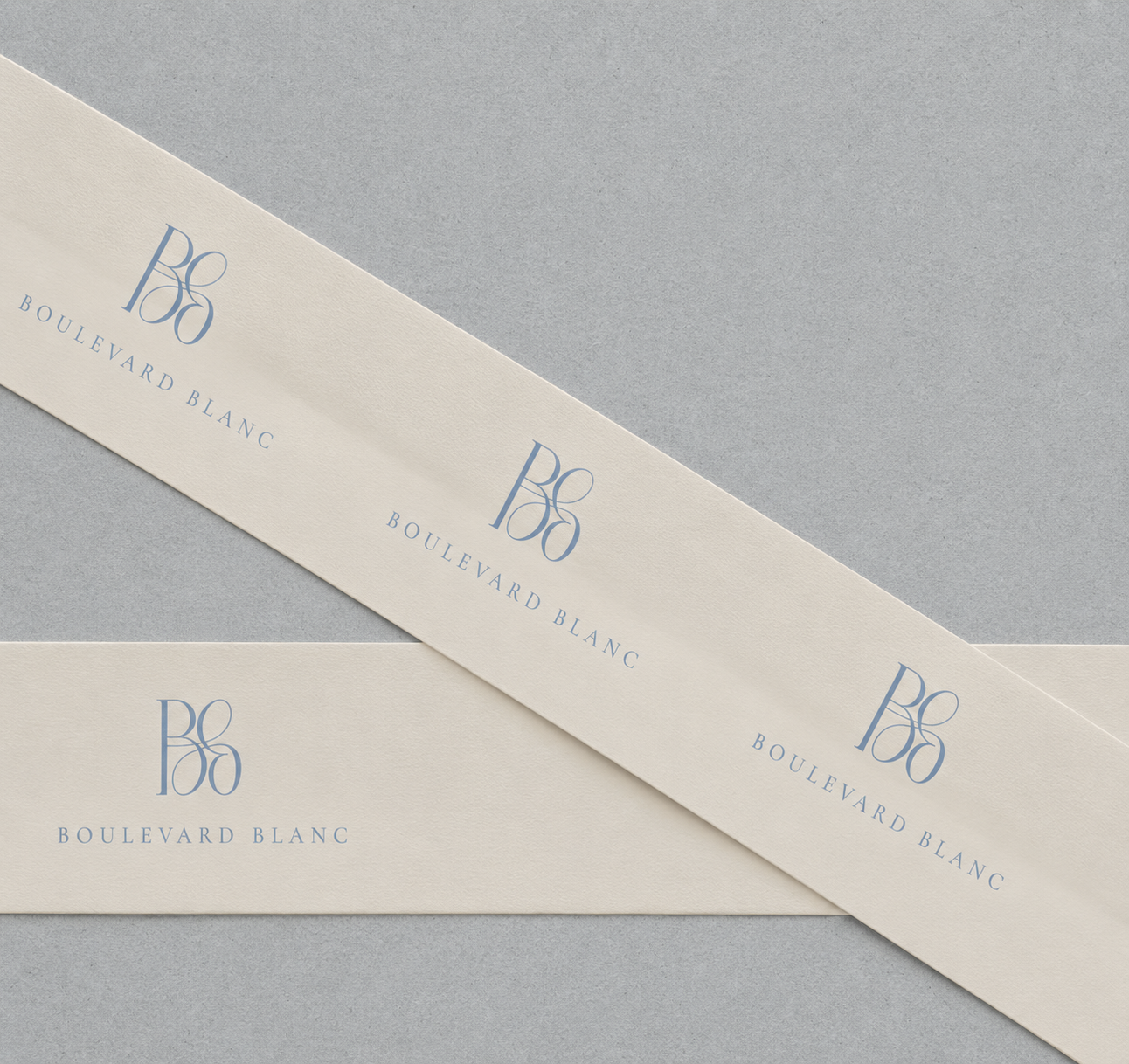 Two cream-colored ribbons with blue text and a logo reading "Boulevard Blanc" placed on a gray surface, one overlapping the other.