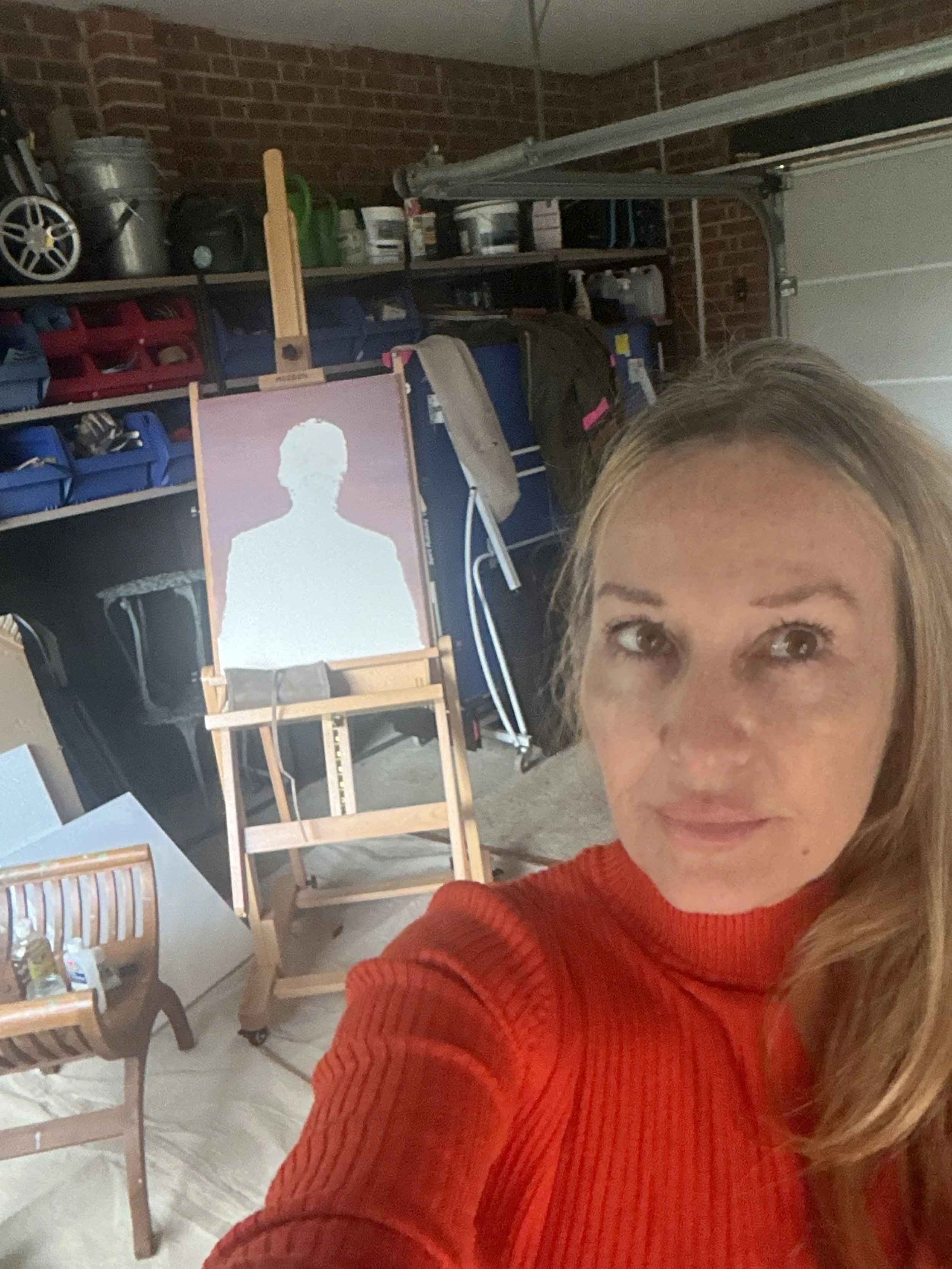 A woman taking a selfie inside a garage, with shelves filled with various containers, tools, and equipment in the background.