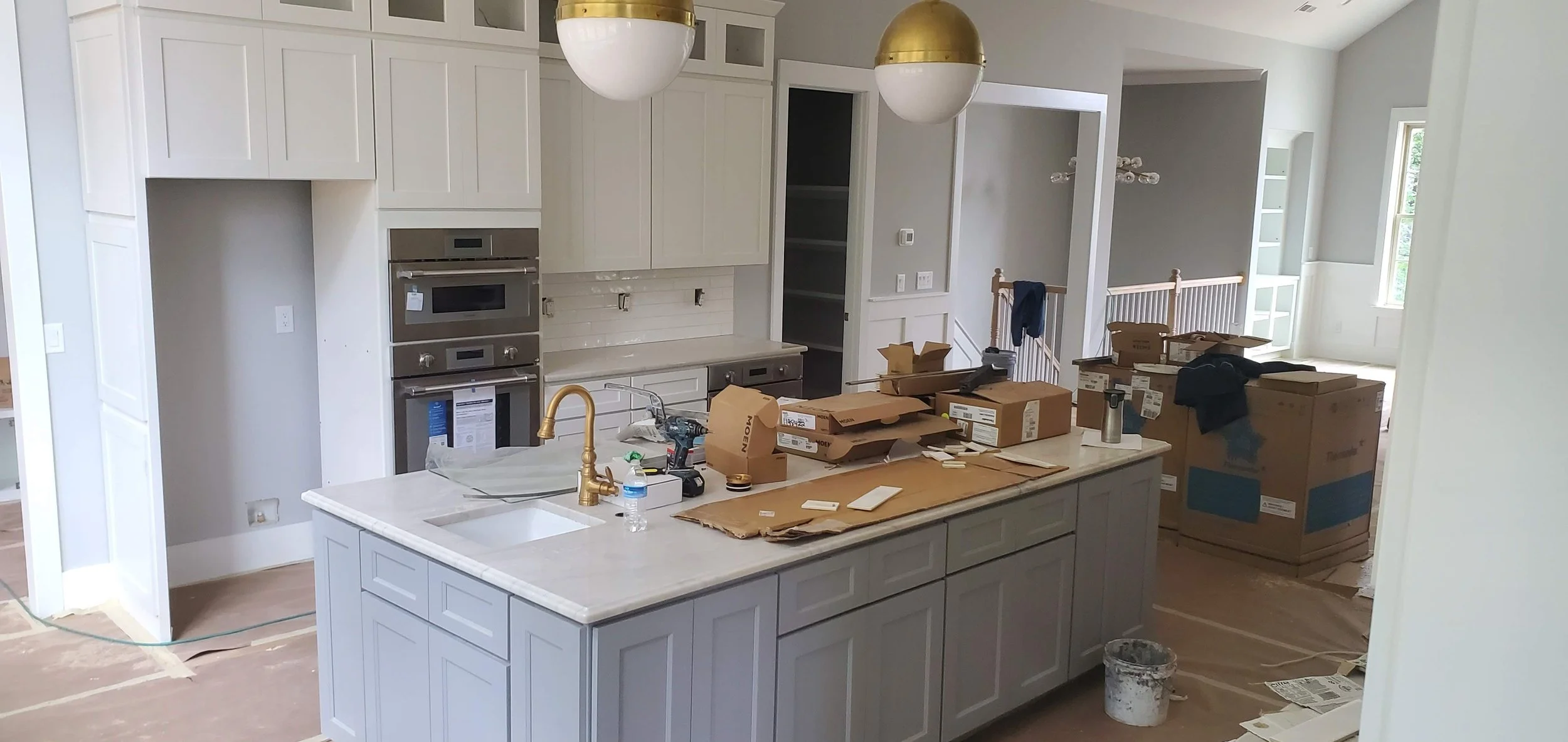 Kitchen under construction with white cabinets, a marble island, and various workshop tools and supplies on the counter and floor.