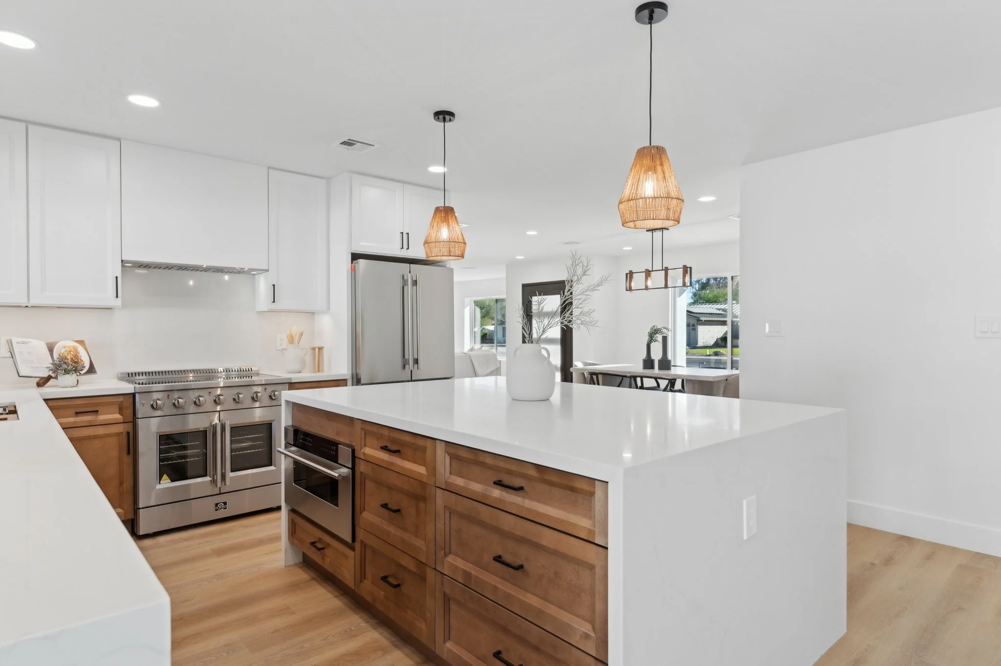 Modern kitchen with white ceilings and walls, wooden cabinets, stainless steel appliances, pendant lights, and large windows.