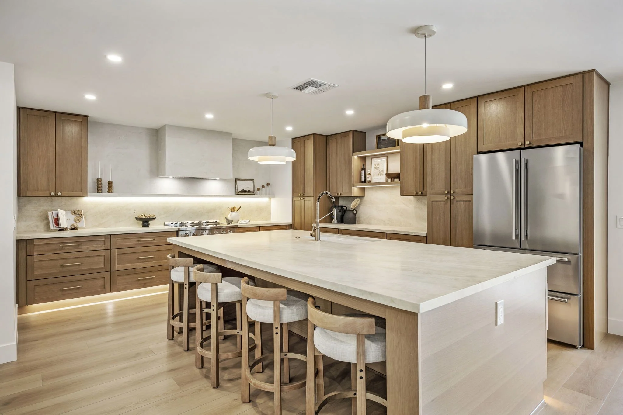 Modern kitchen with wooden cabinets, a large island with a light-colored countertop, and pendant lights hanging from the ceiling.