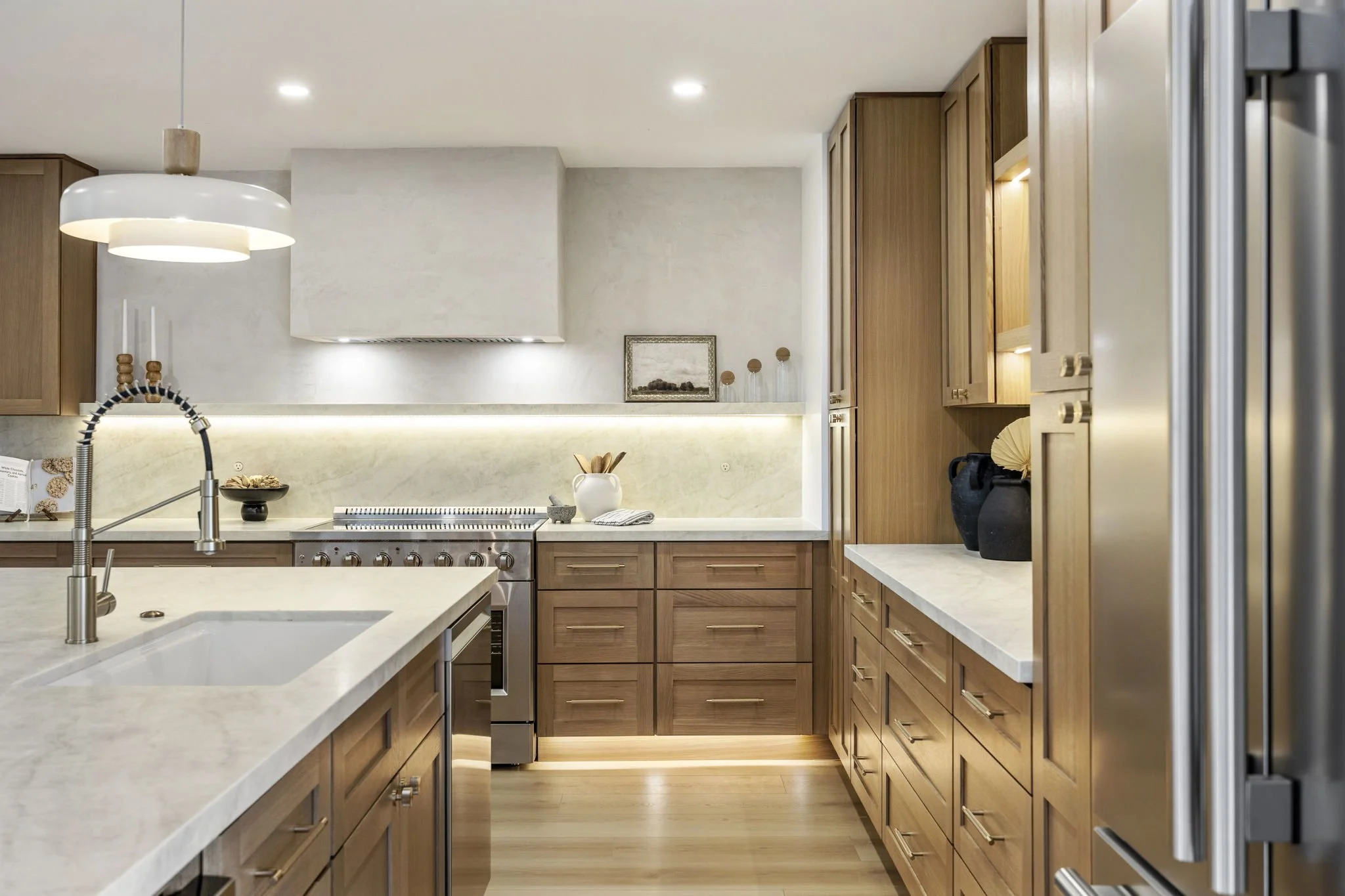 A modern kitchen with wooden cabinets, a white countertop, a stainless steel oven, and decorative items on the counter, including black vases and a white pitcher.