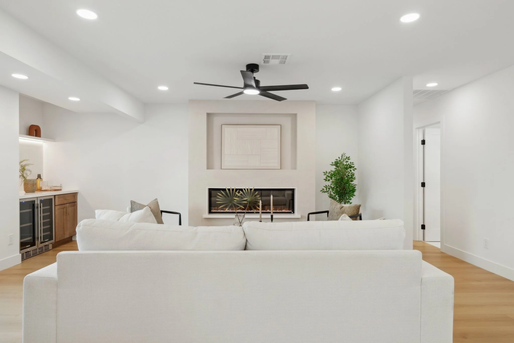 Living room with white sofa, fireplace, ceiling fan, potted plant, and modern decor.
