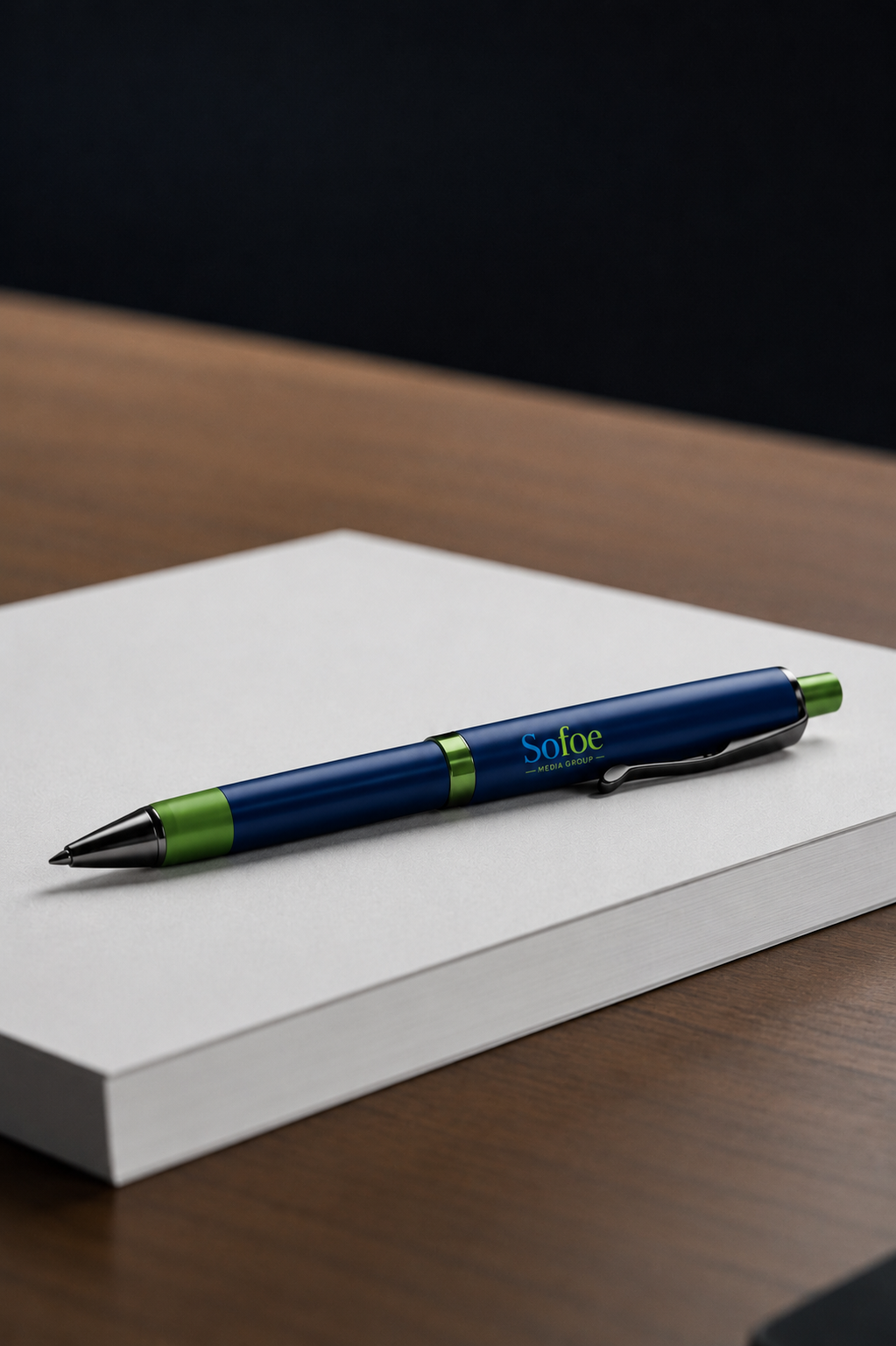 A branded blue and green retractable pen resting on a blank white notepad on a wooden desk.