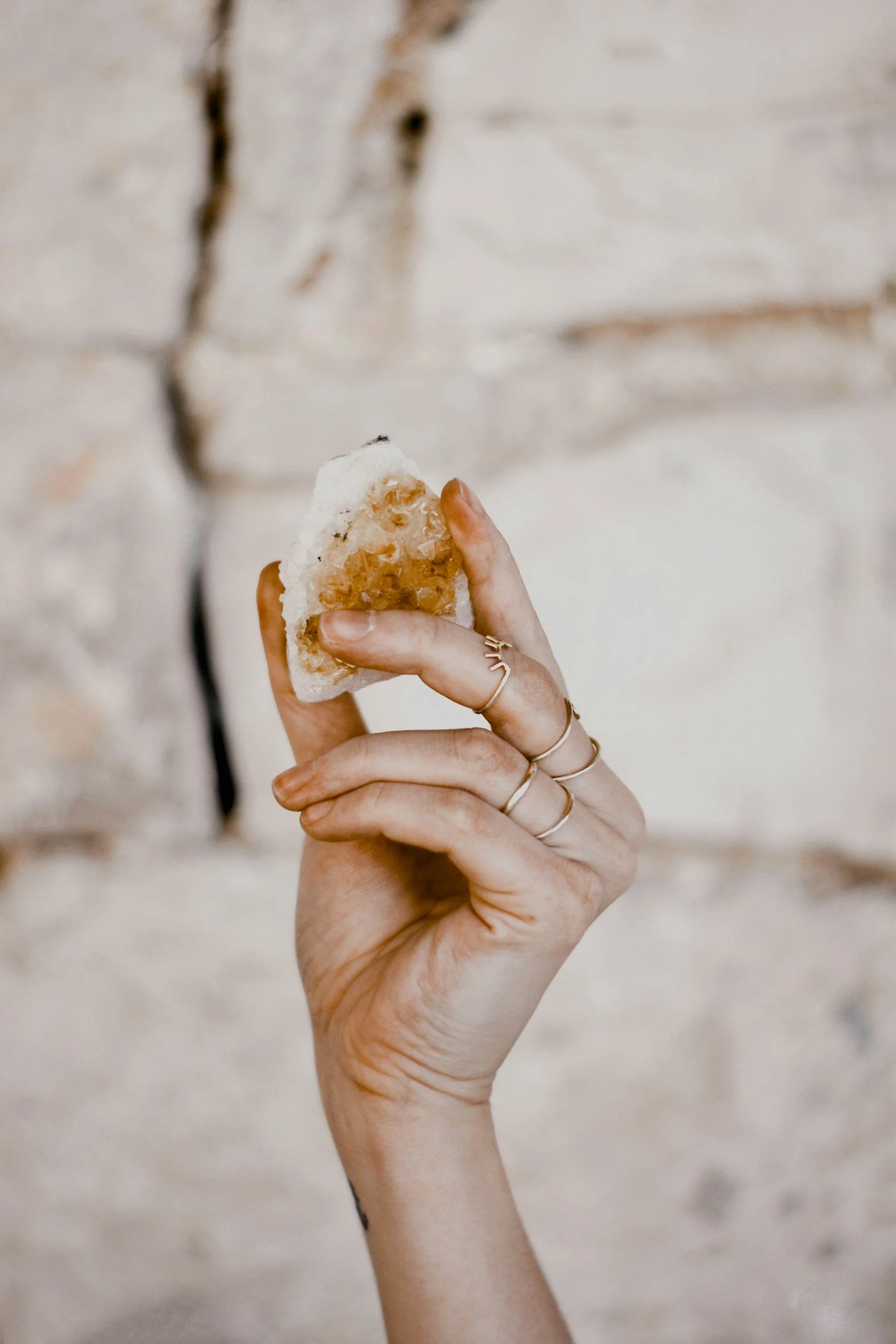Person holding a piece of crystal with a blurred light-colored brick wall background.