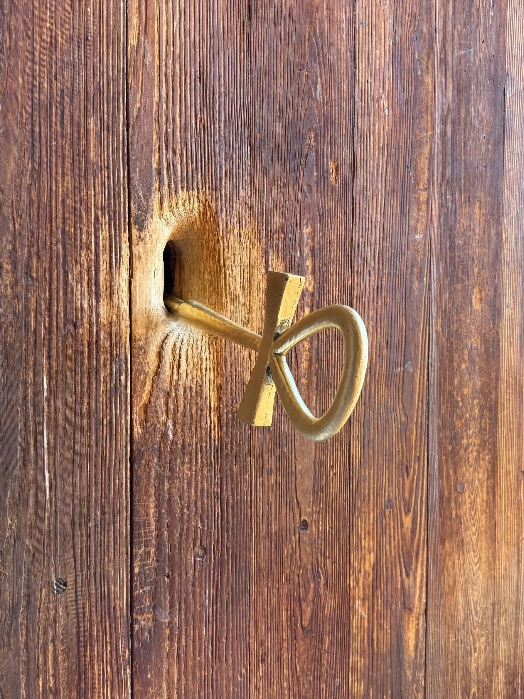 A golden-colored vintage key with a decorative bow and a thick shank placed on a wooden surface.