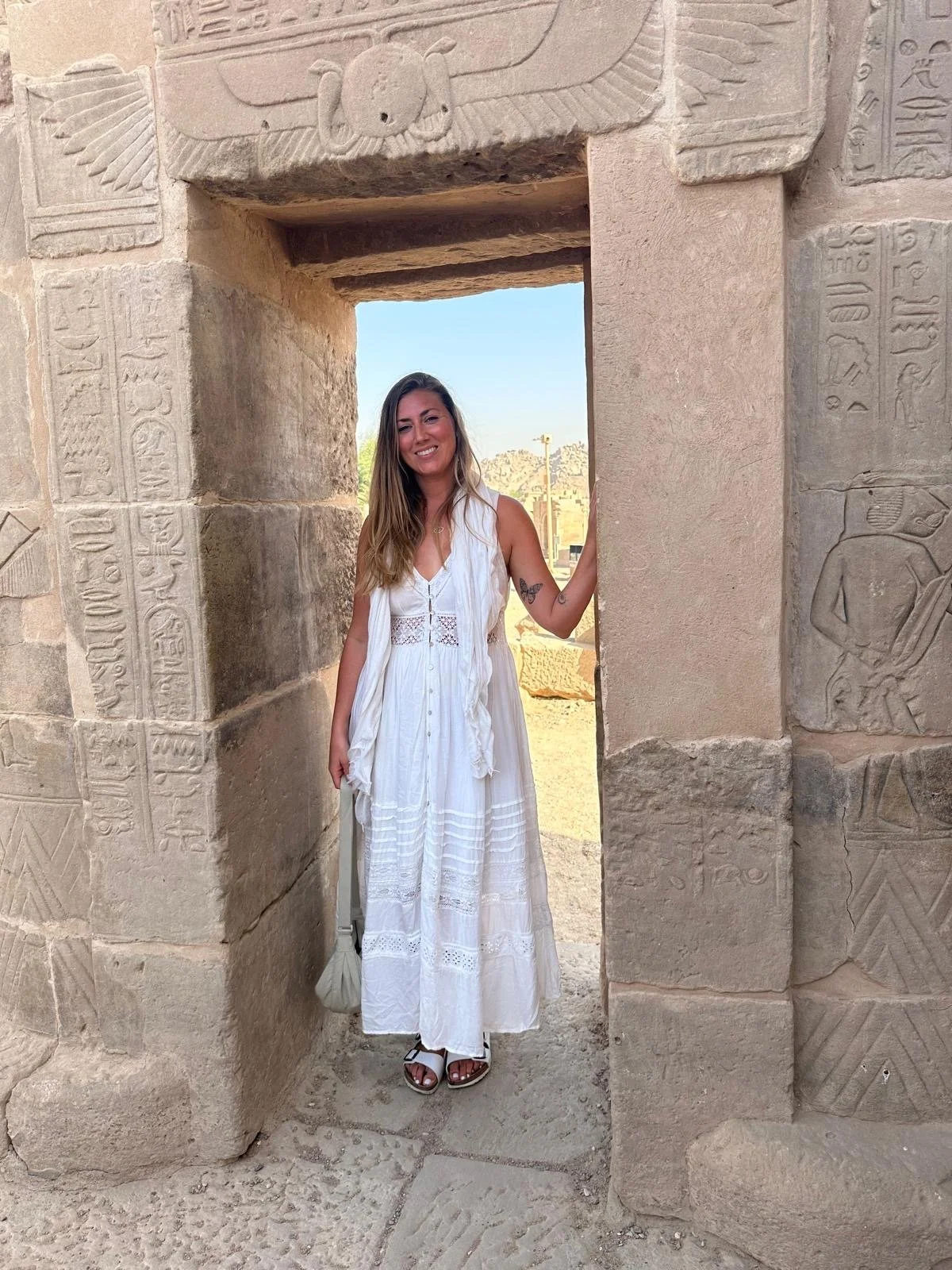 A woman in a white dress stands in an ancient Egyptian temple doorway, surrounded by carved hieroglyphs and stone sculptures.