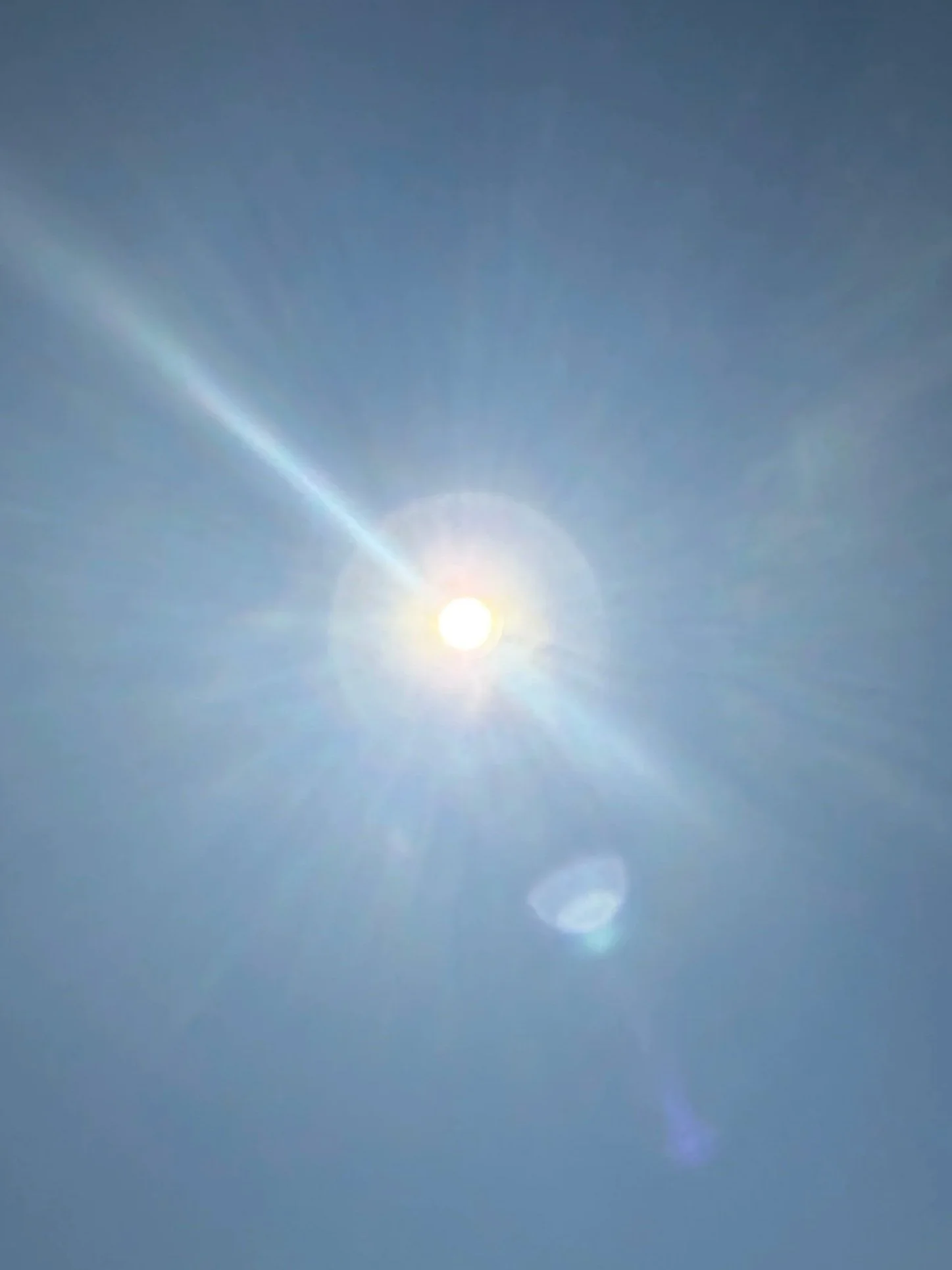 Bright sun in a clear blue sky with lens flare and minimal clouds