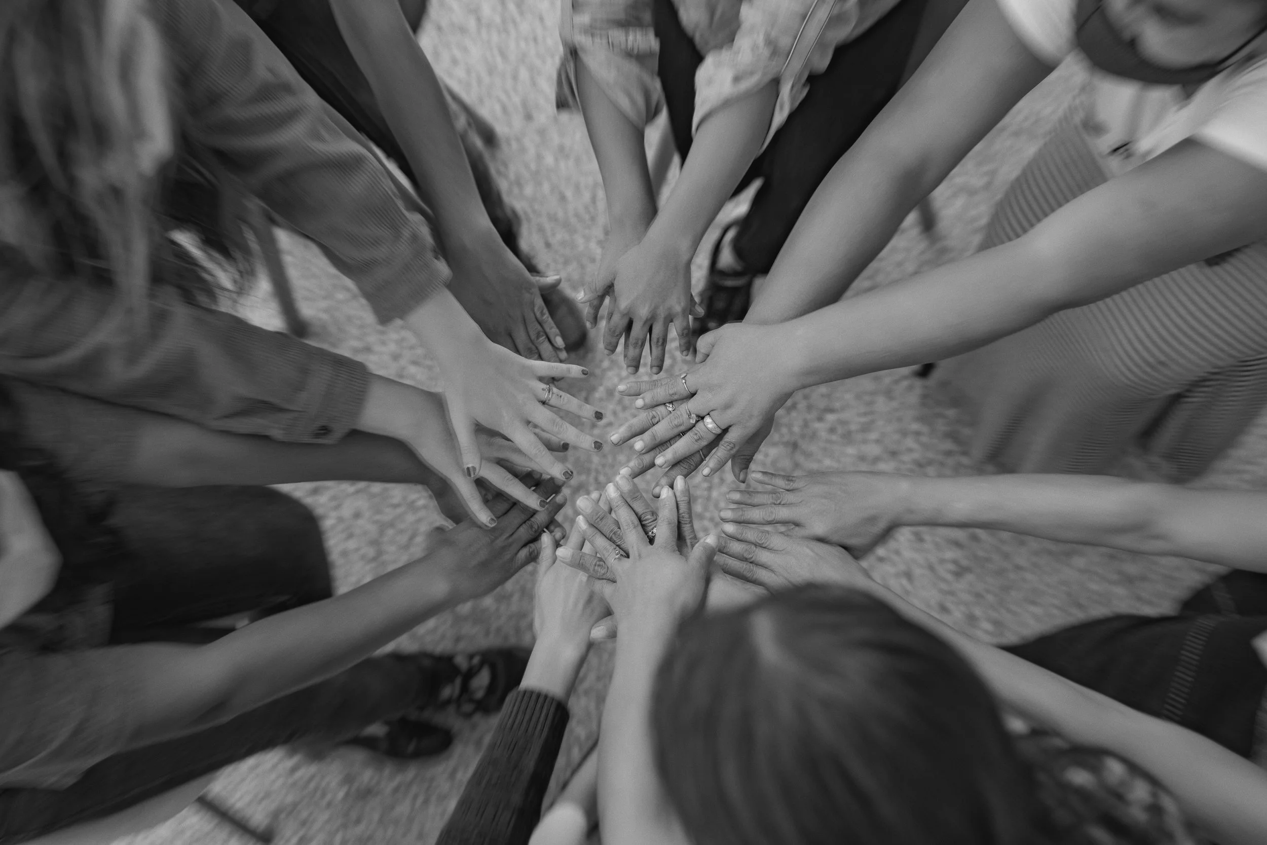 A black-and-white photo shows multiple hands from diverse individuals touching in the center, symbolizing unity and teamwork.