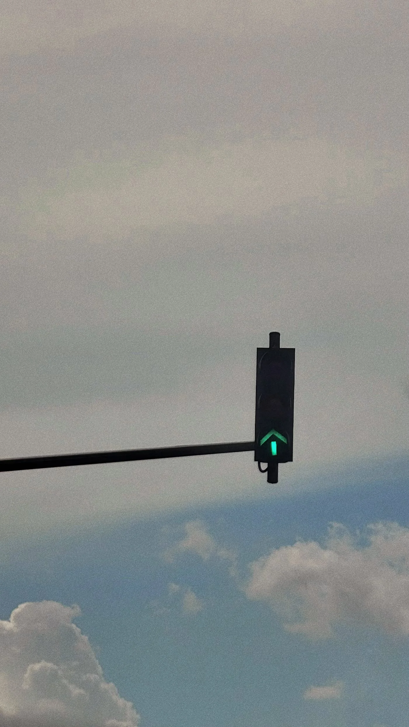 Traffic light with a green arrow pointing upward against a cloudy sky.